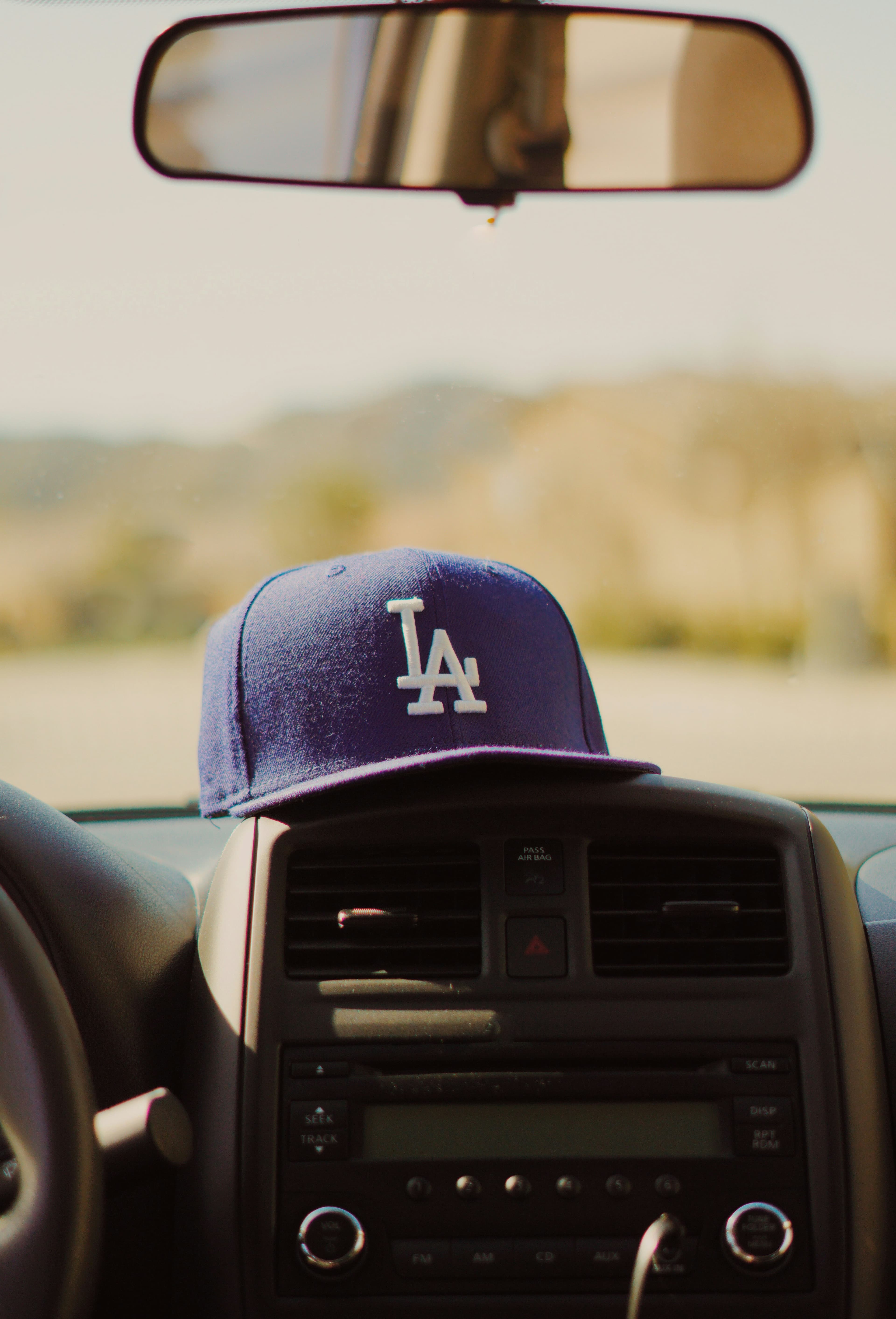 A blue Dodgers hat that says LA sitting on a car dashboard driving in the desert.