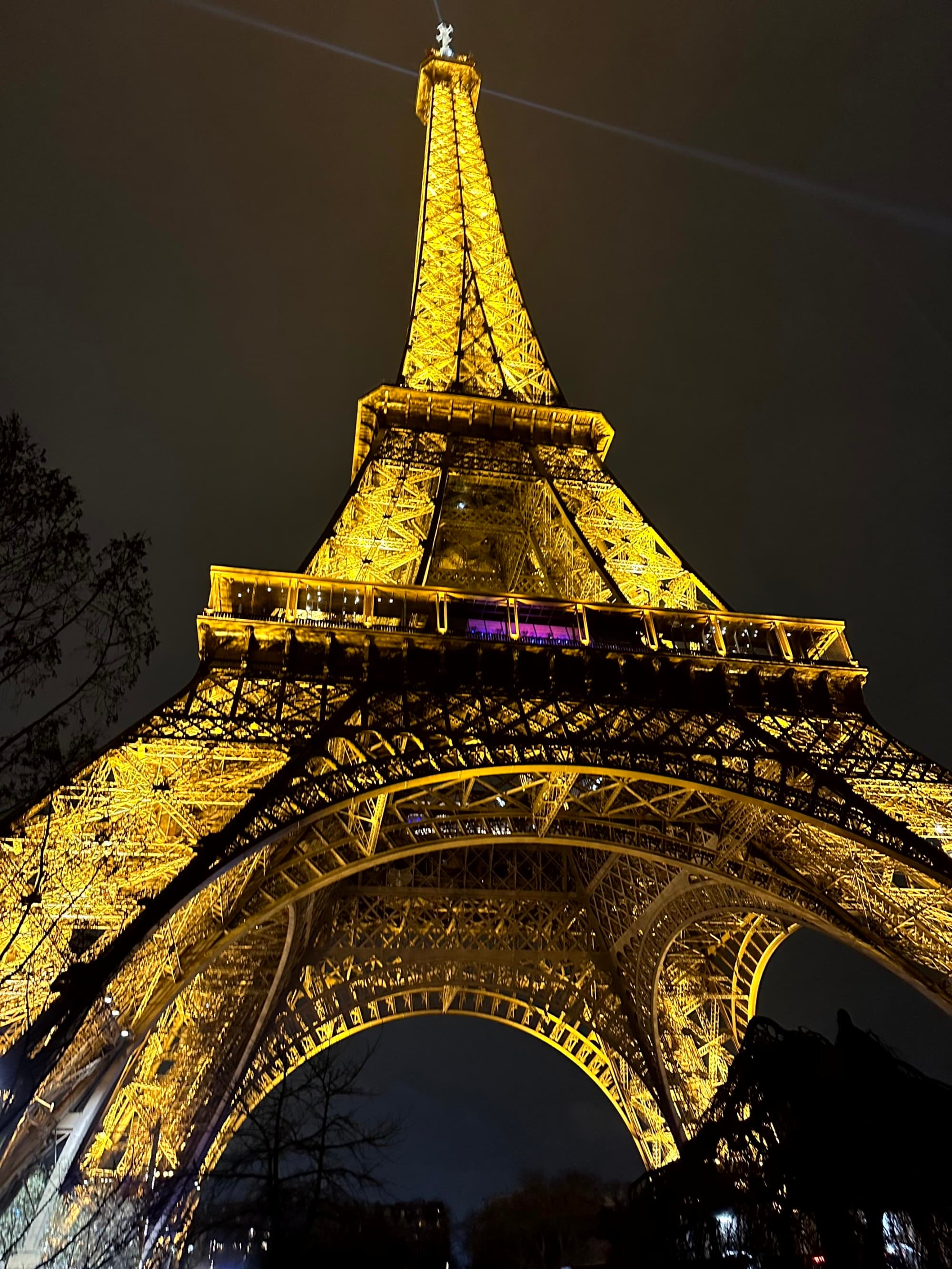 A view of the iconic Eiffel Tower illuminated at night from underneath.