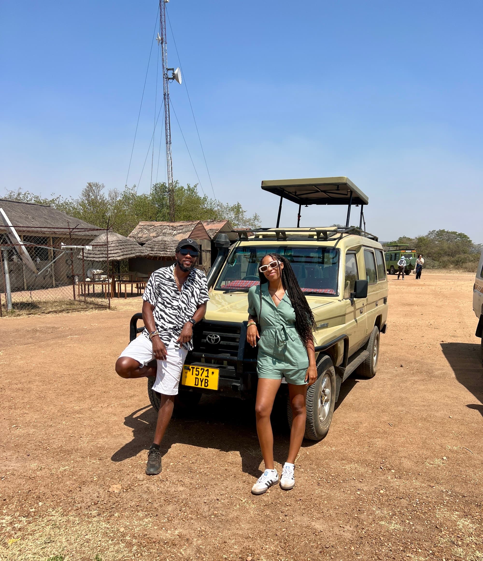 Two individuals in front of a safari vehicle during the daytime.