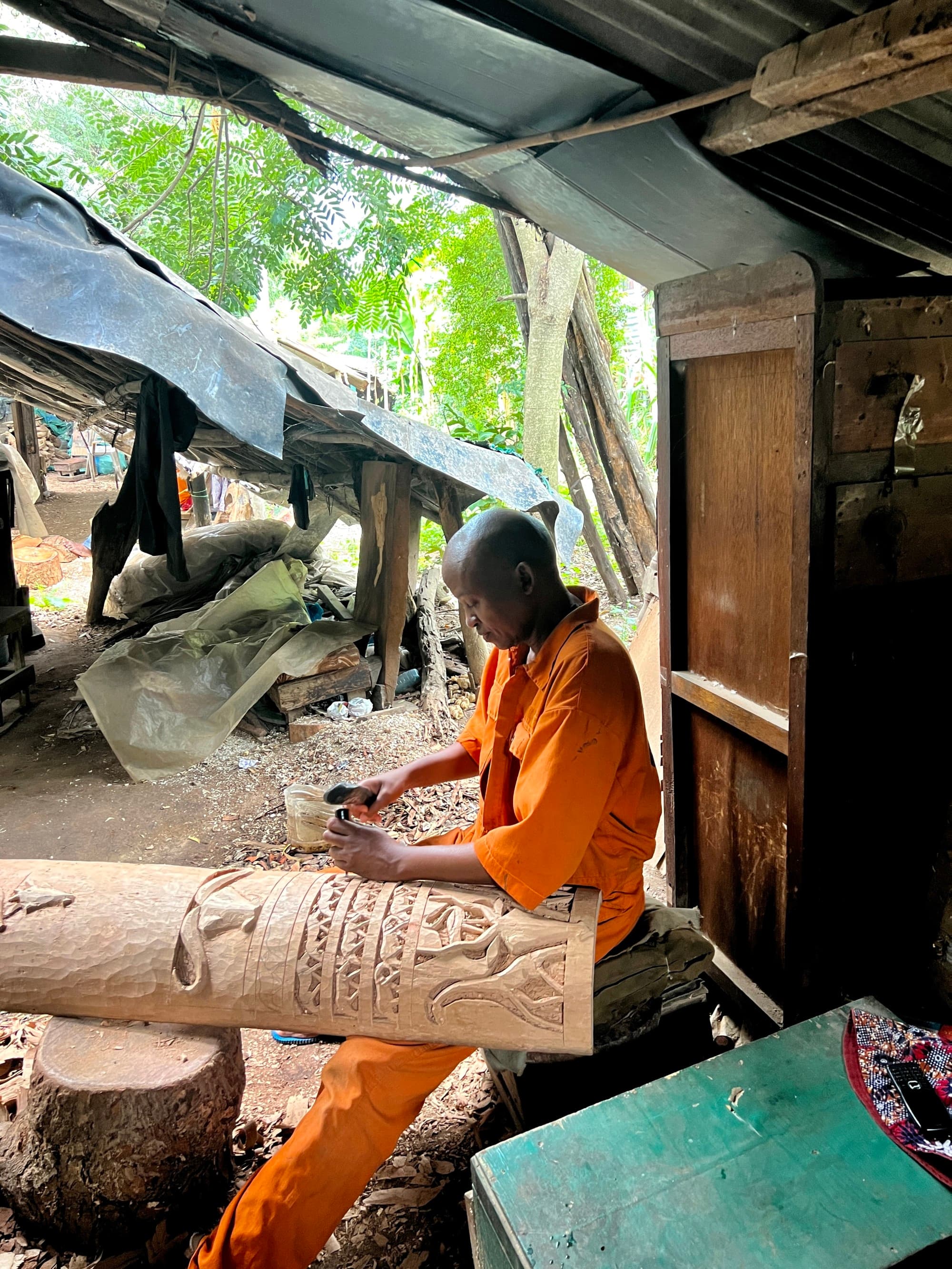 A man in orange clothes carving a wood log.