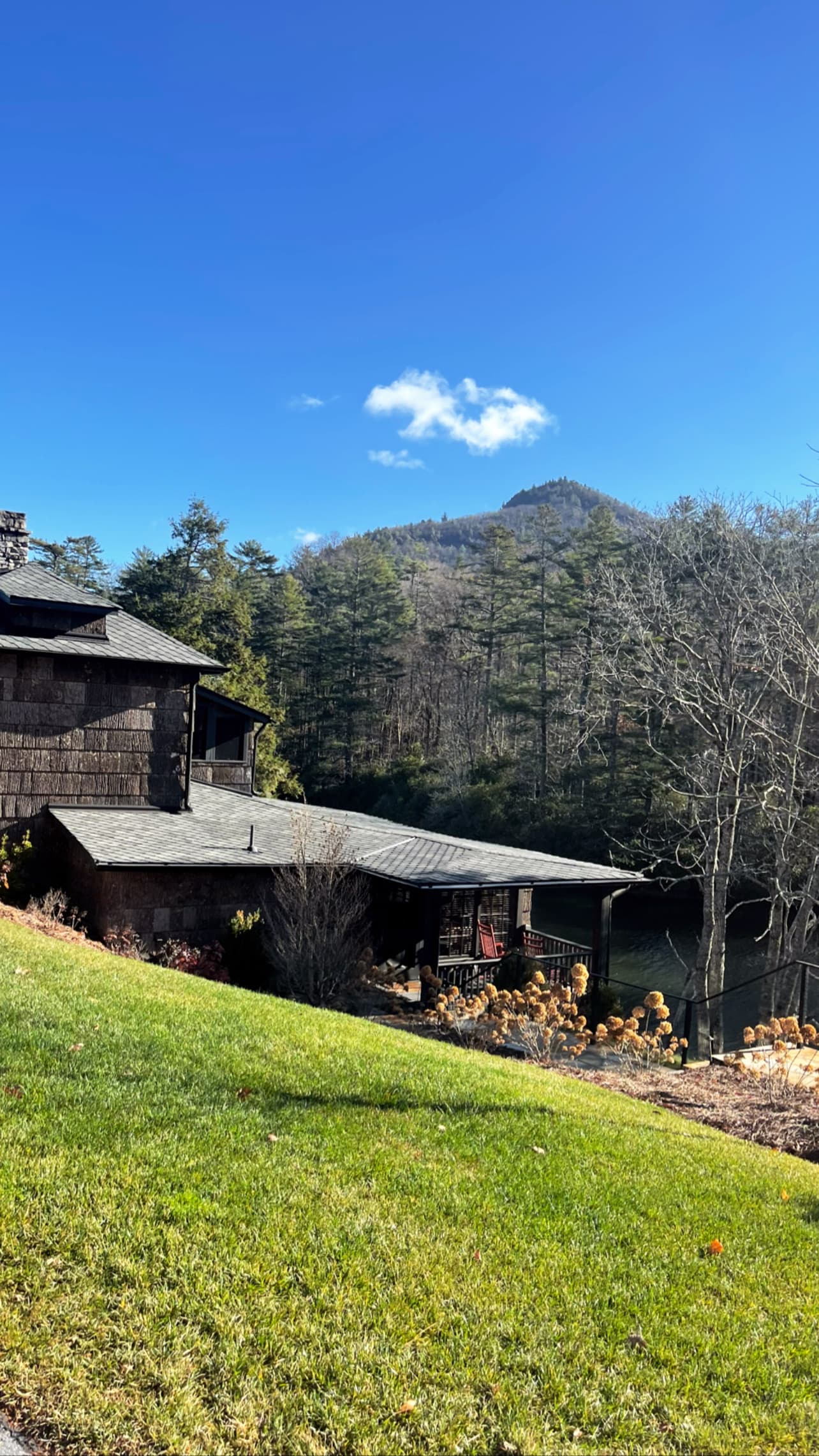 A beautiful view of a green hillside with a cabin-style building surrounded by trees and greenery on a sunny day.