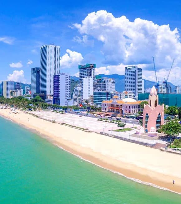 A view of the coastline of Nha Trang Beach with tall, modern buildings and turquoise colored waters.