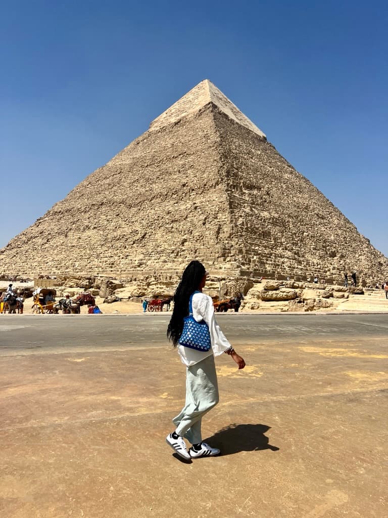 A woman standing in front of a pyramid on a sunny day.