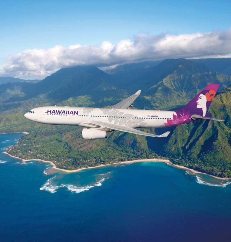 A Hawaiian airlines airplane in flight over beautiful island scenery on a clear day