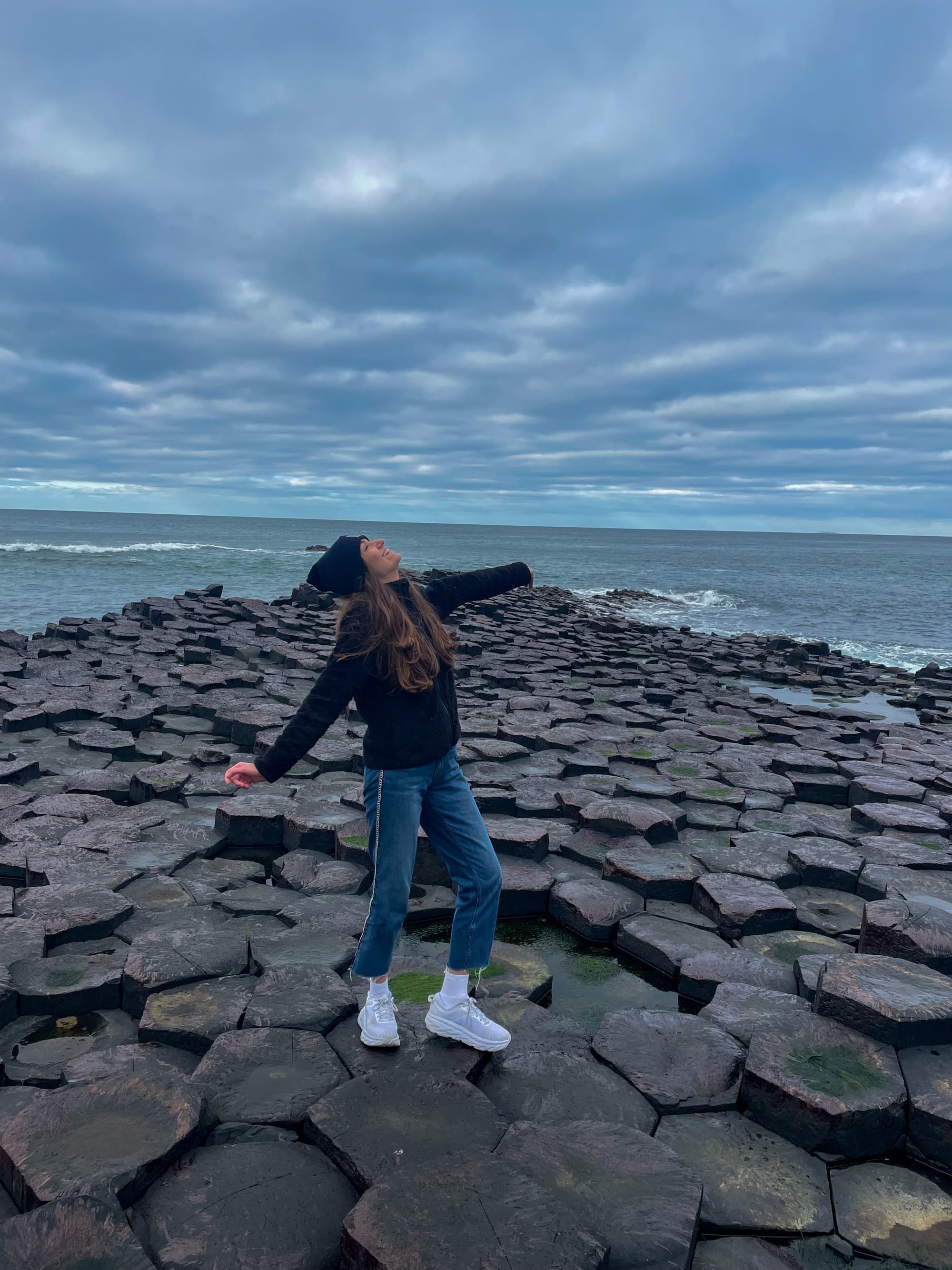 A person stands on the Giant’s Causeway in Northern Ireland, arms outstretched amidst the unique hexagonal rock formations.