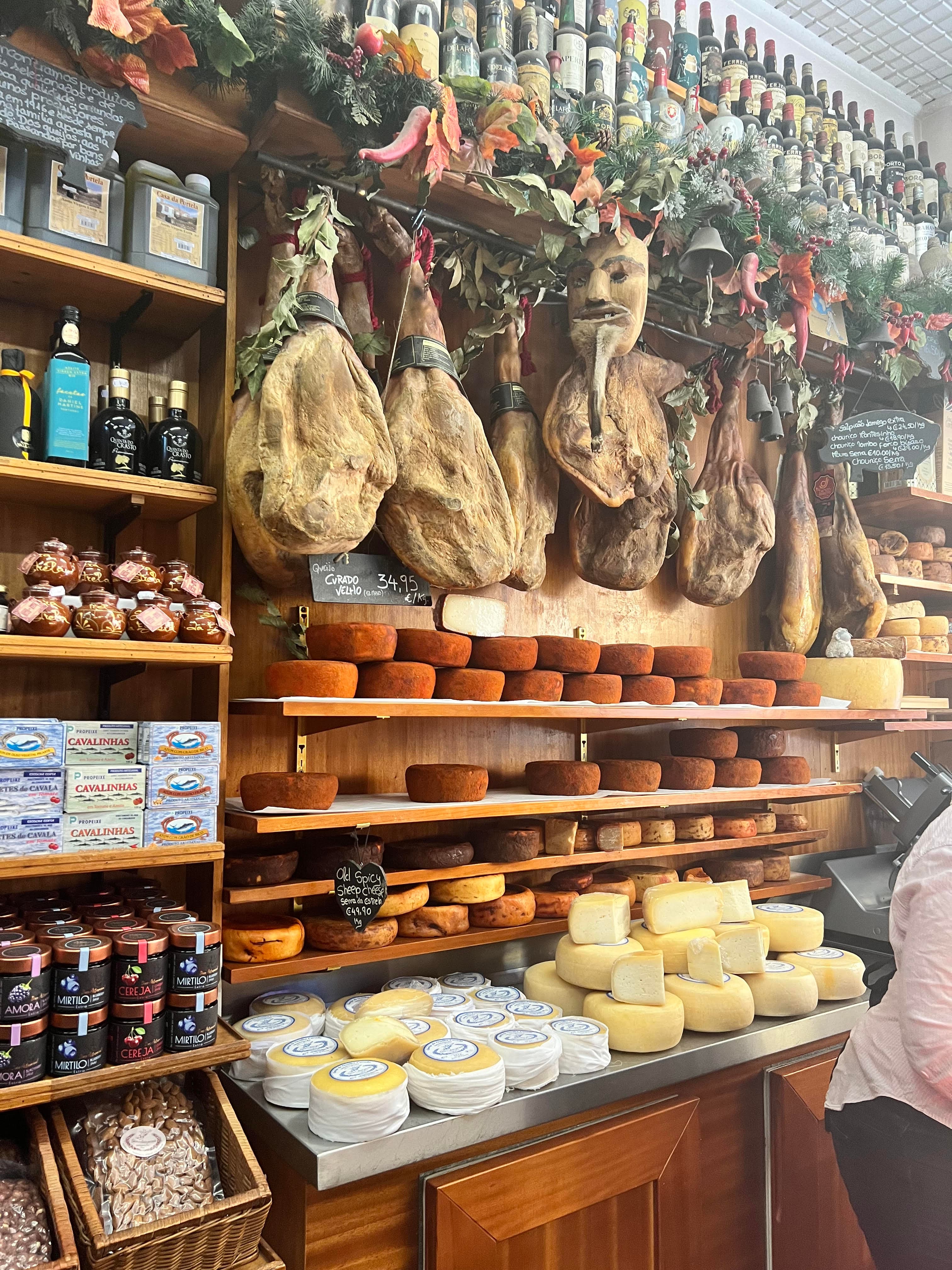 A shop wall with shelves of cheese and meat.
