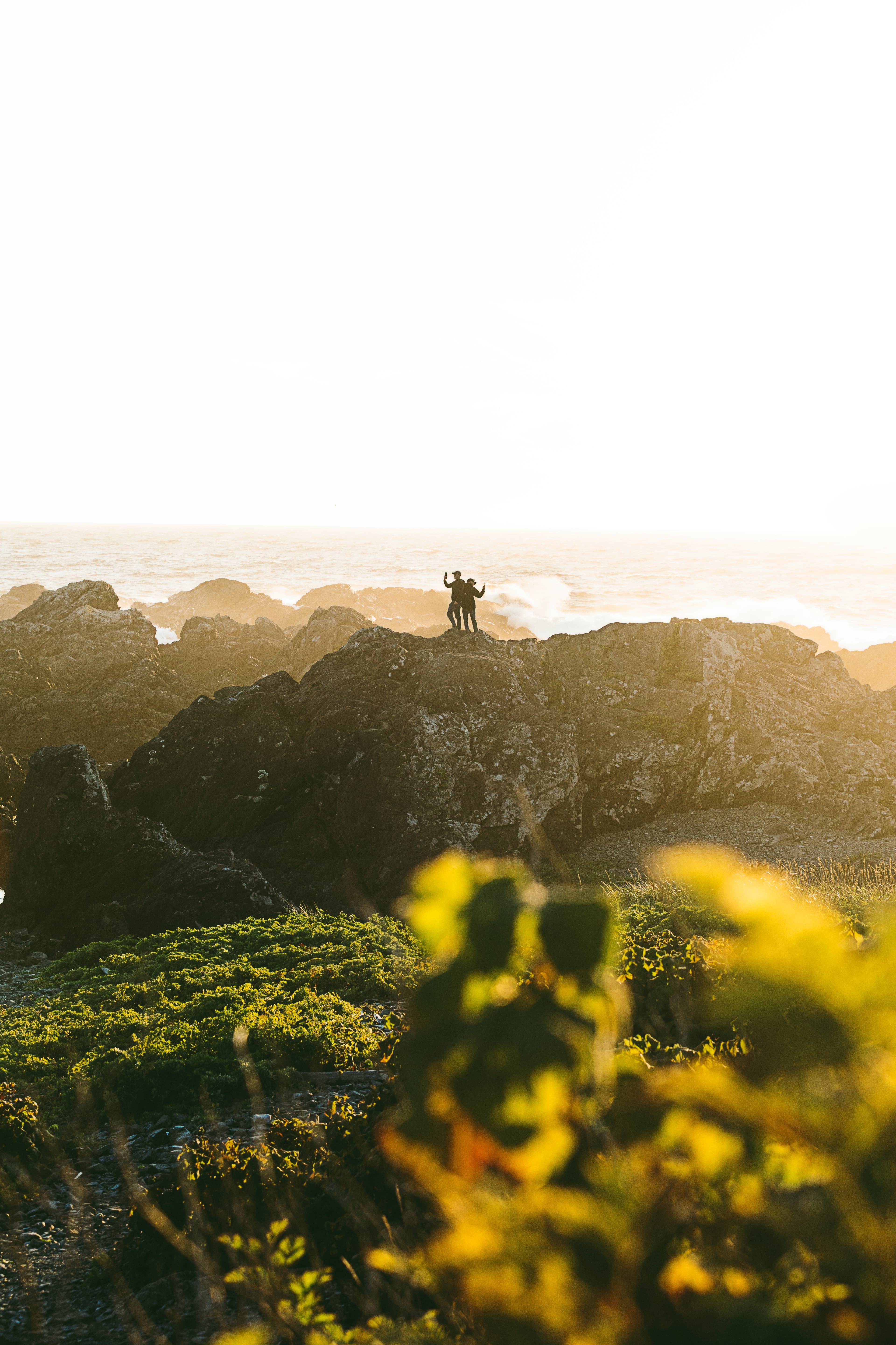 Two people standing on rocks at sunset.