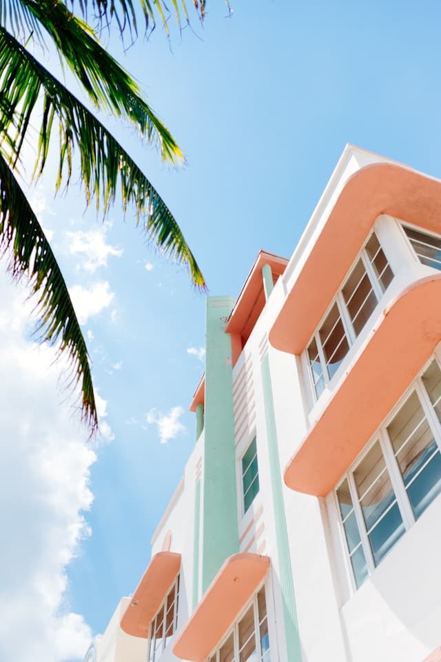A low angle shot of a white and peach-colored, residential building, and leaves from a palm tree in Miami.