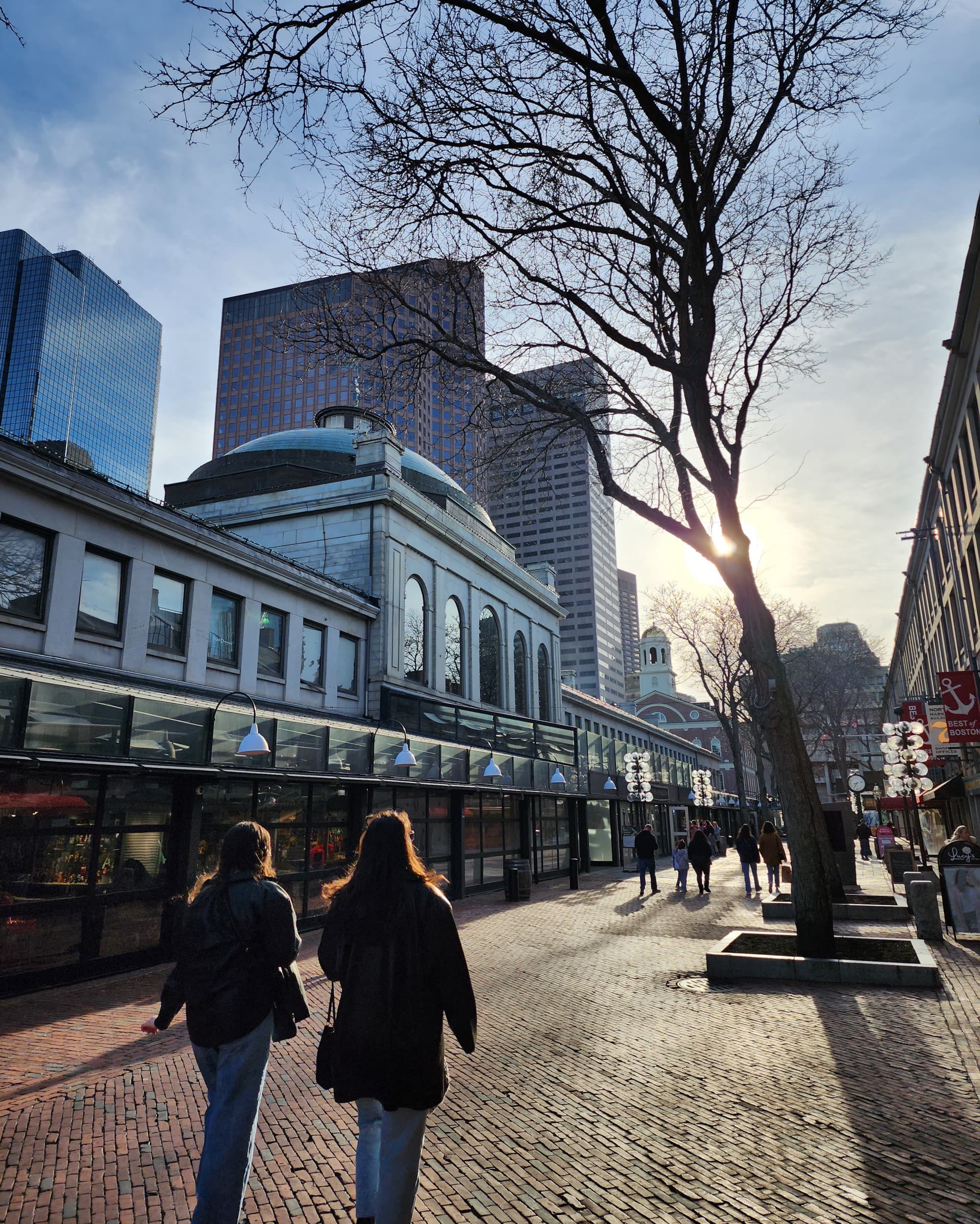 The image portrays a bustling city scene with pedestrians and buildings, bathed in sunlight from a clear sky.