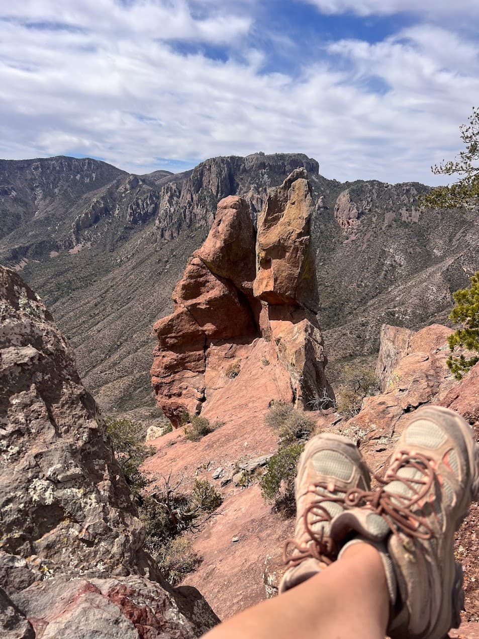 A photo of a person's legs crossed at the top of a hiking trail with a view of the valley in the distance