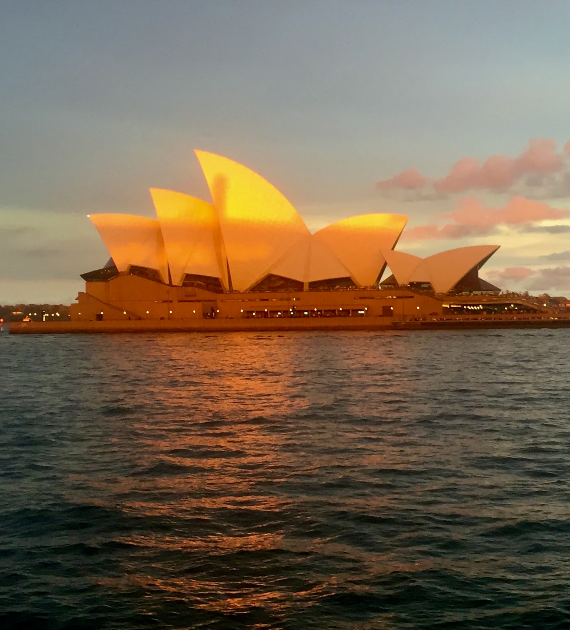 A golden sun setting over the Sydney Opera House and Harbour.