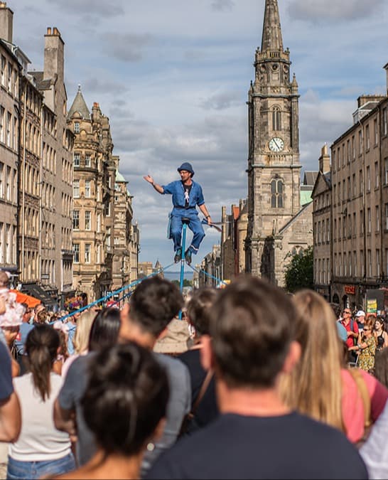 A man sitting on stilts in front of a crowd in a city street