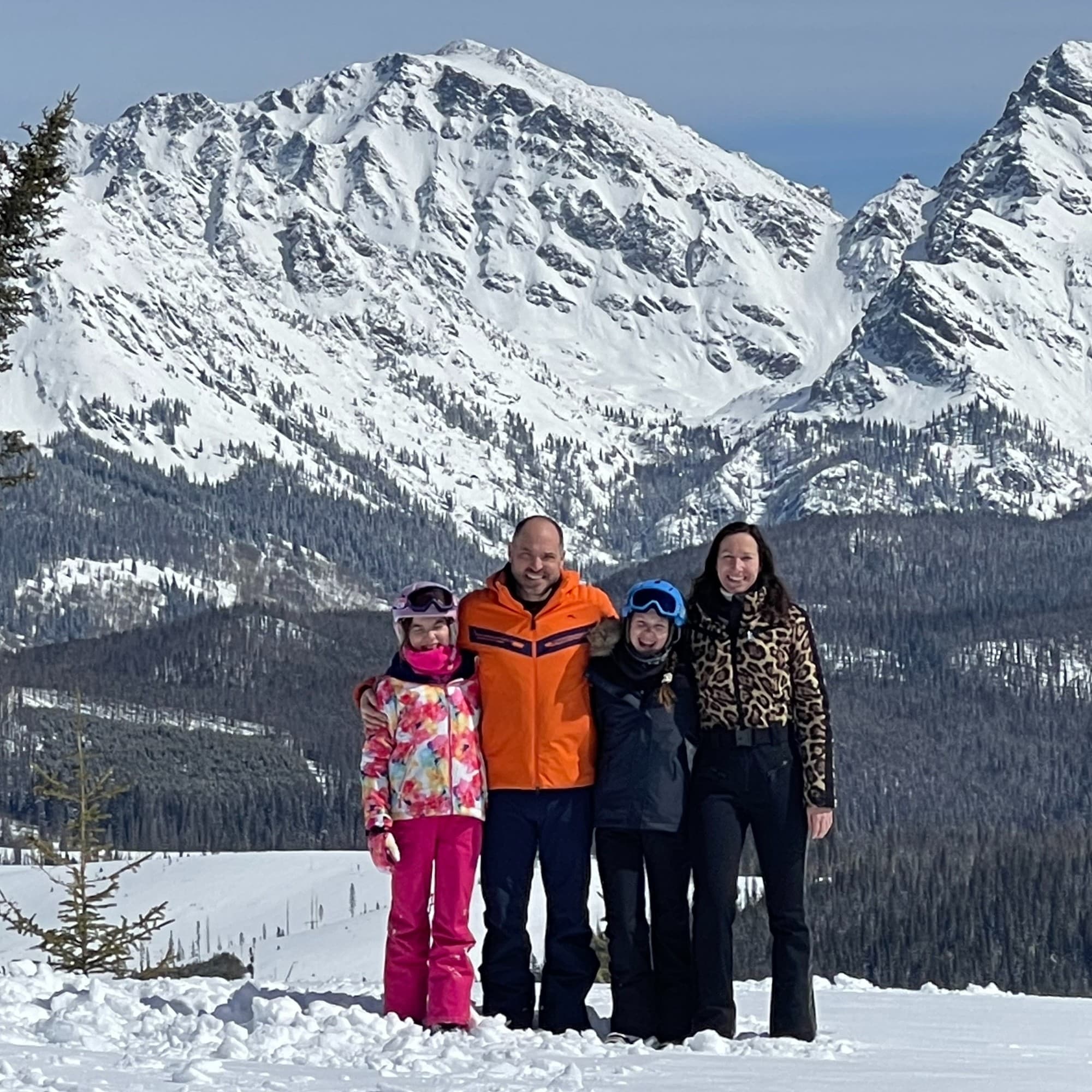 A picture of a family posing in front of a snowy mountain during the daytime.