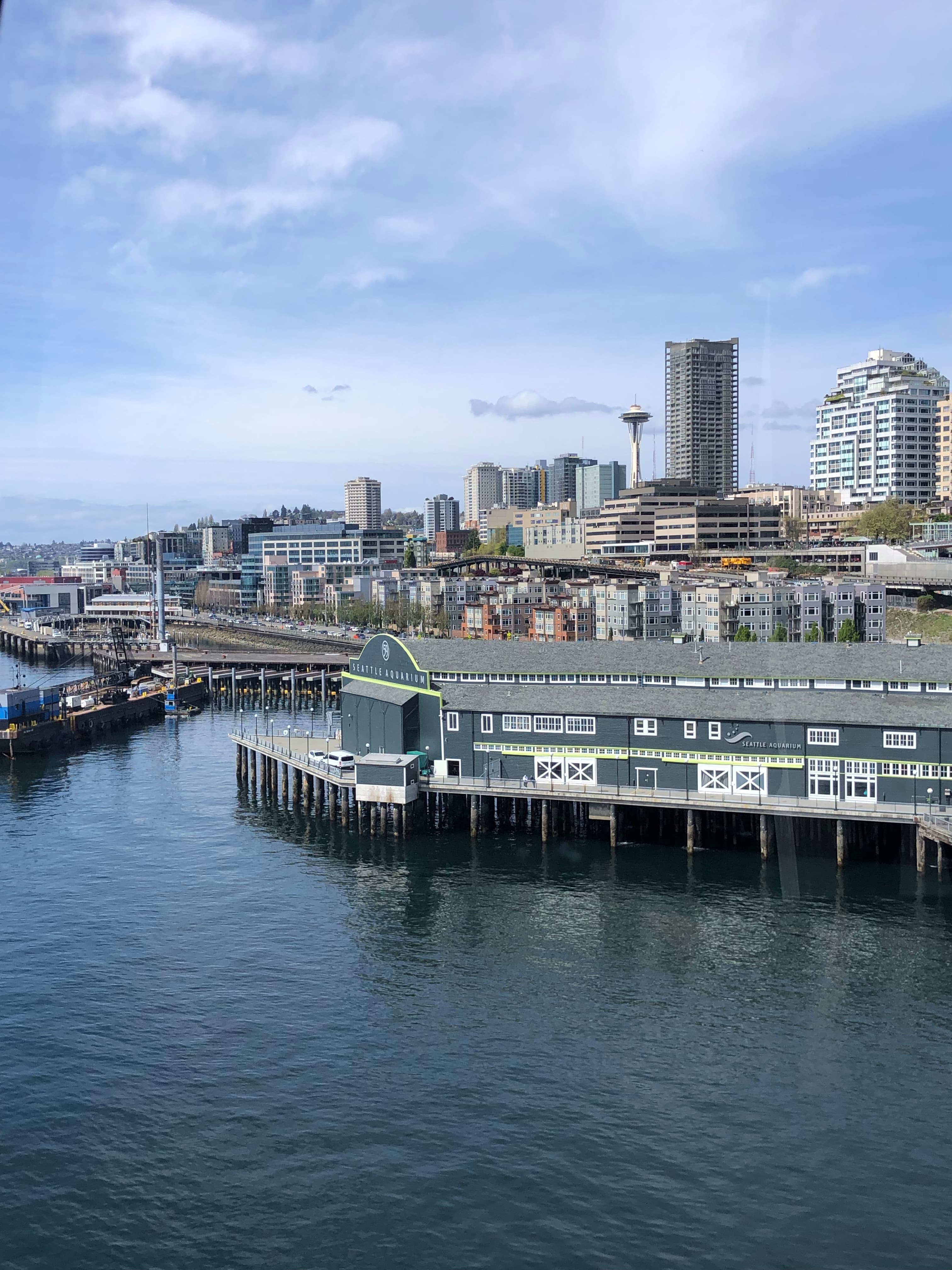 An aerial view of Seattle's skyline with the Seattle Aquarium in the forefront on a sunny day.