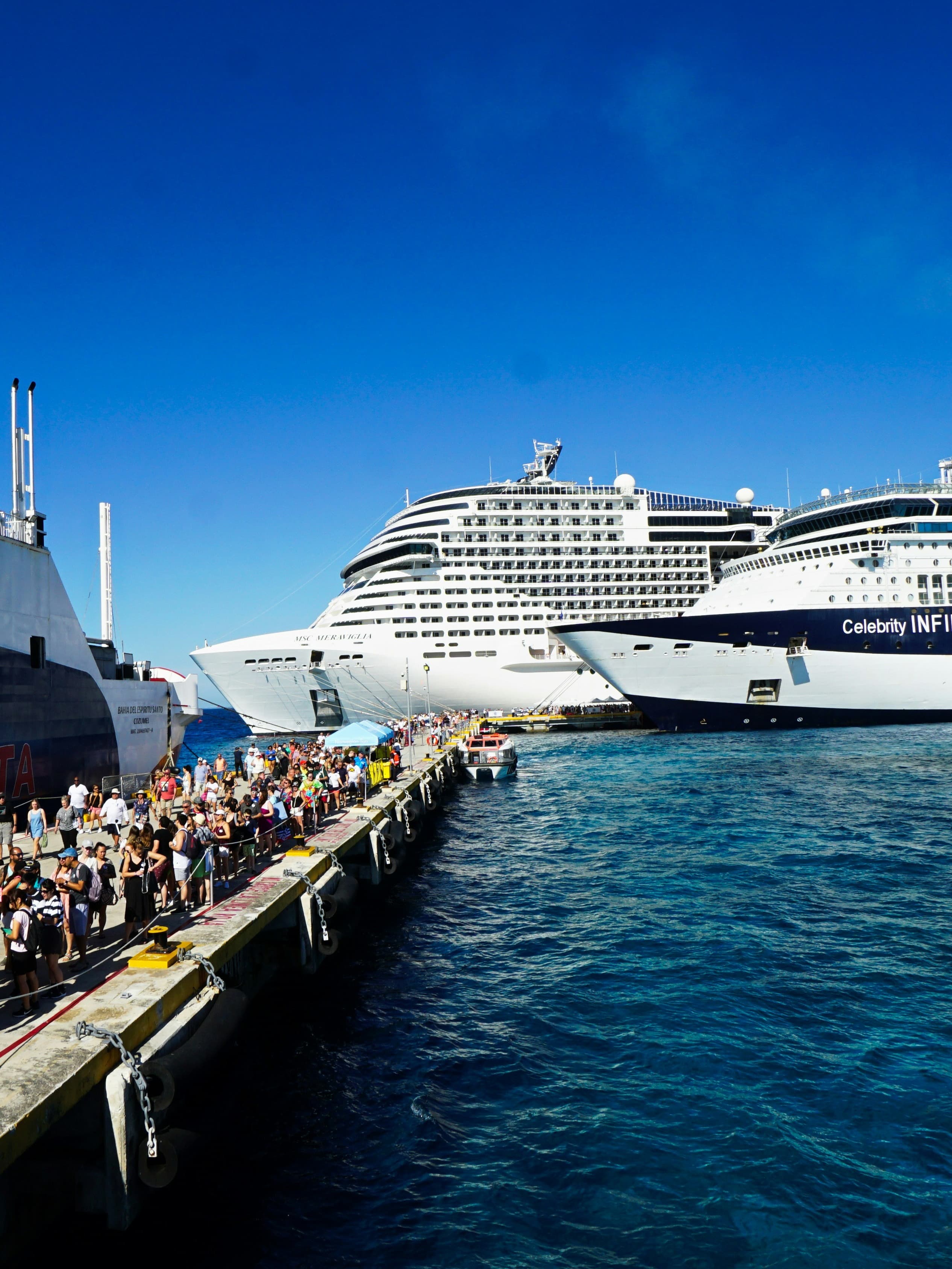 Travelers on the dock by cruise ships on the water.