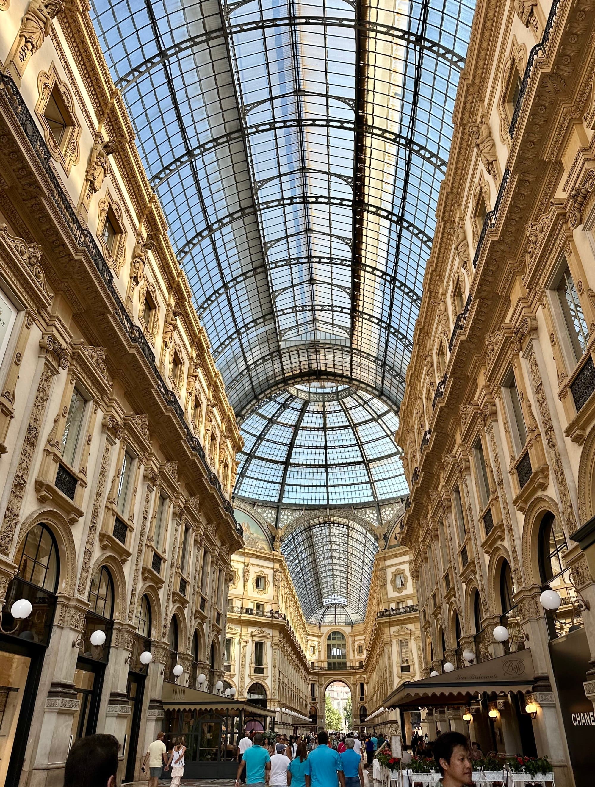 The image features an ornate gallery with a glass dome ceiling, bustling with visitors and lined with shops.