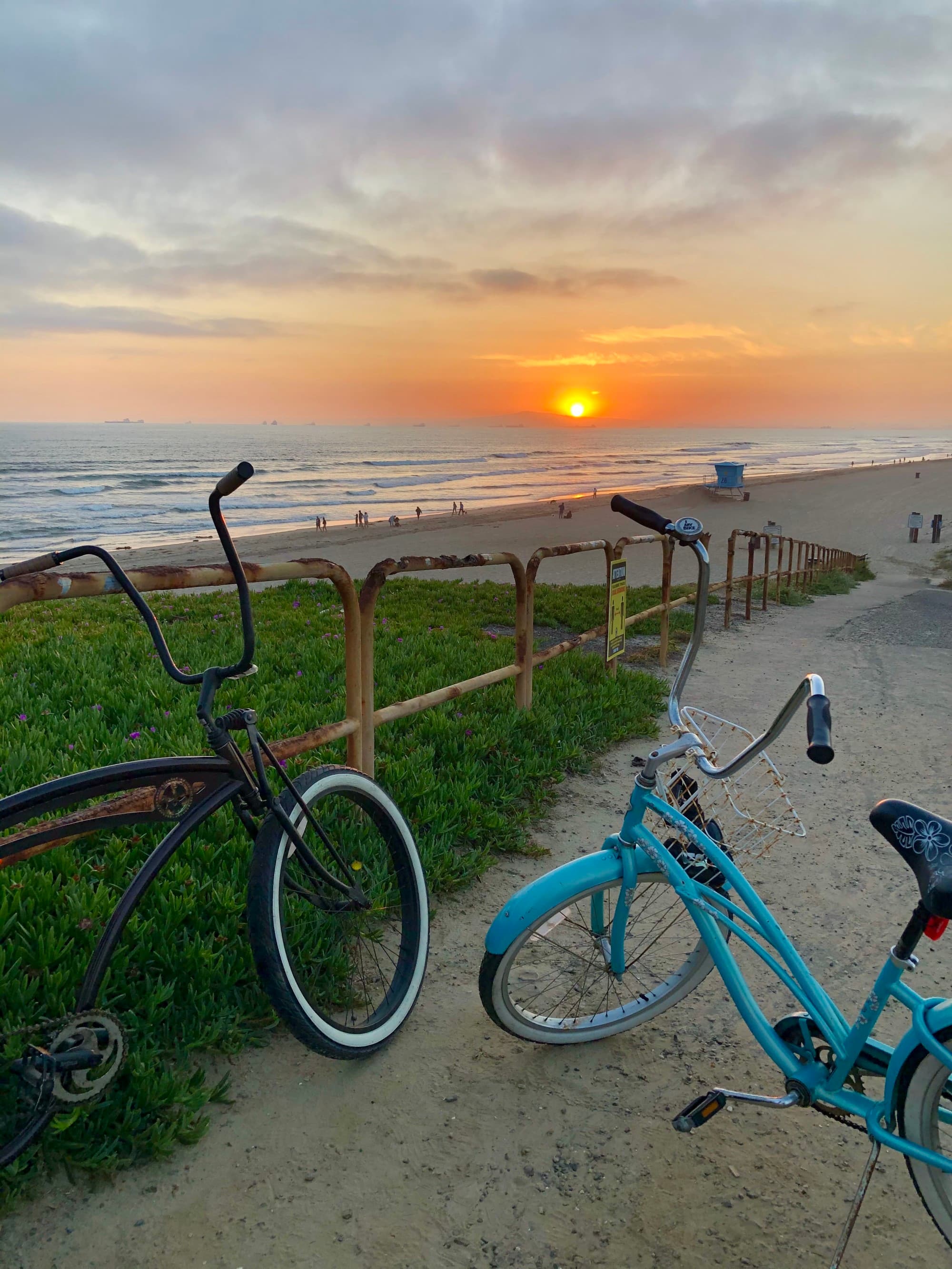 The image captures a tranquil beach sunset with two bicycles poised to enjoy the view.