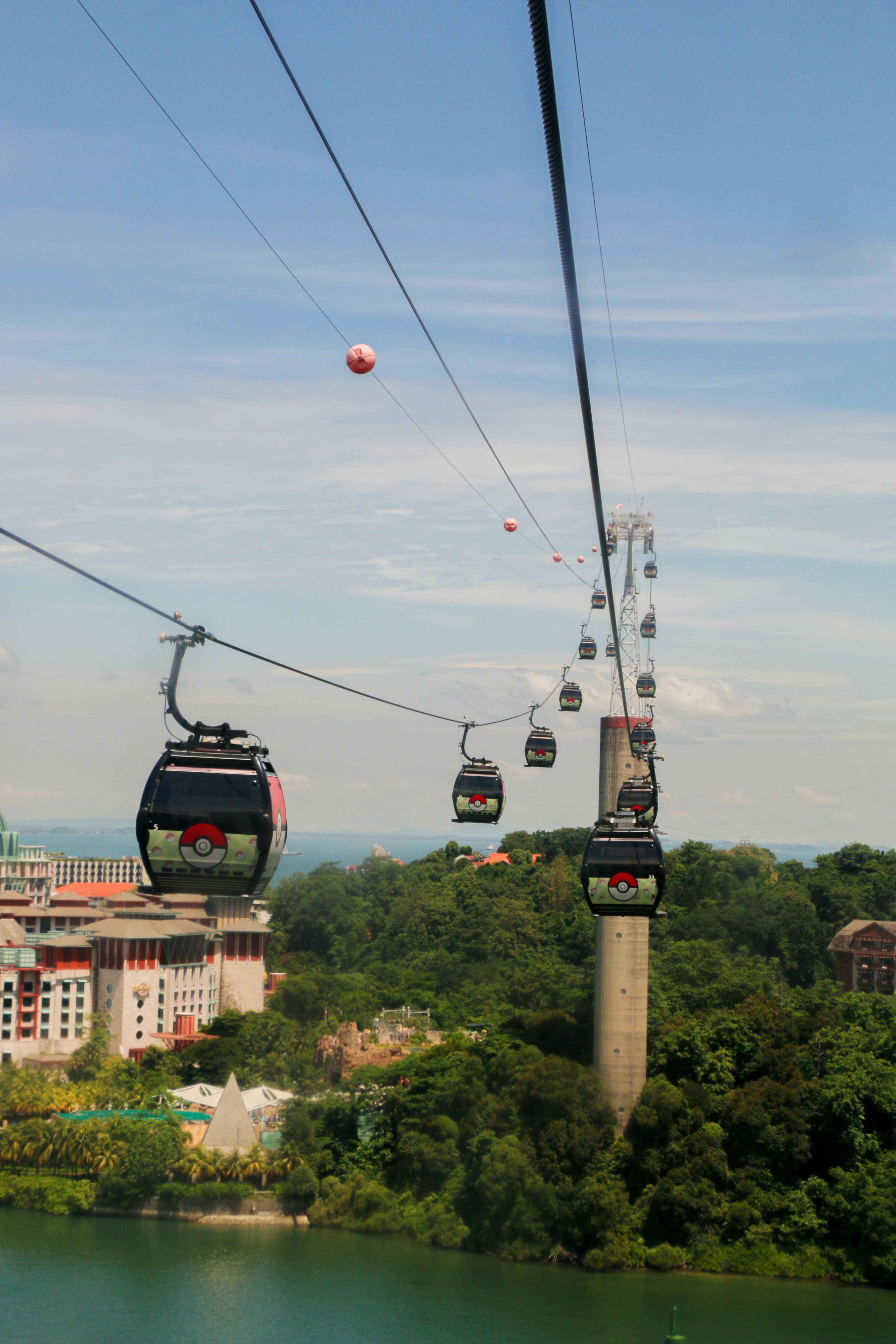 A view of gondolas traveling over the water to Sentosa Island, with trees and Universal Studios in the distance.