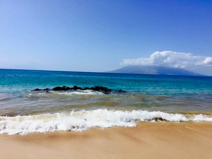 A view of a Maui beach, the sand, blue water, and sunny sky.