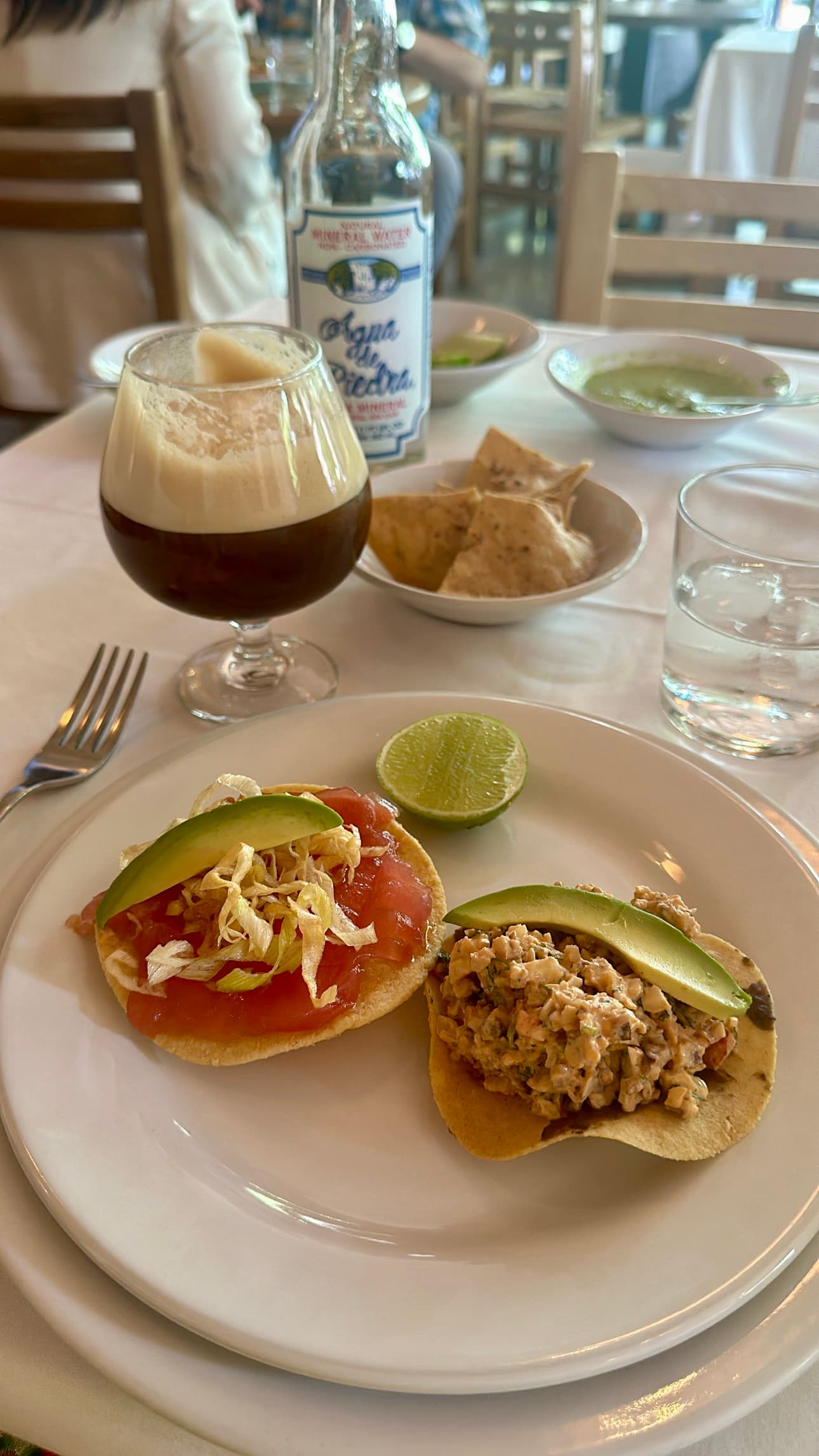 A plate of open freshly made tostadas, a glass of a dark, frothy beer, and other side dishes on the table of a restaurant.