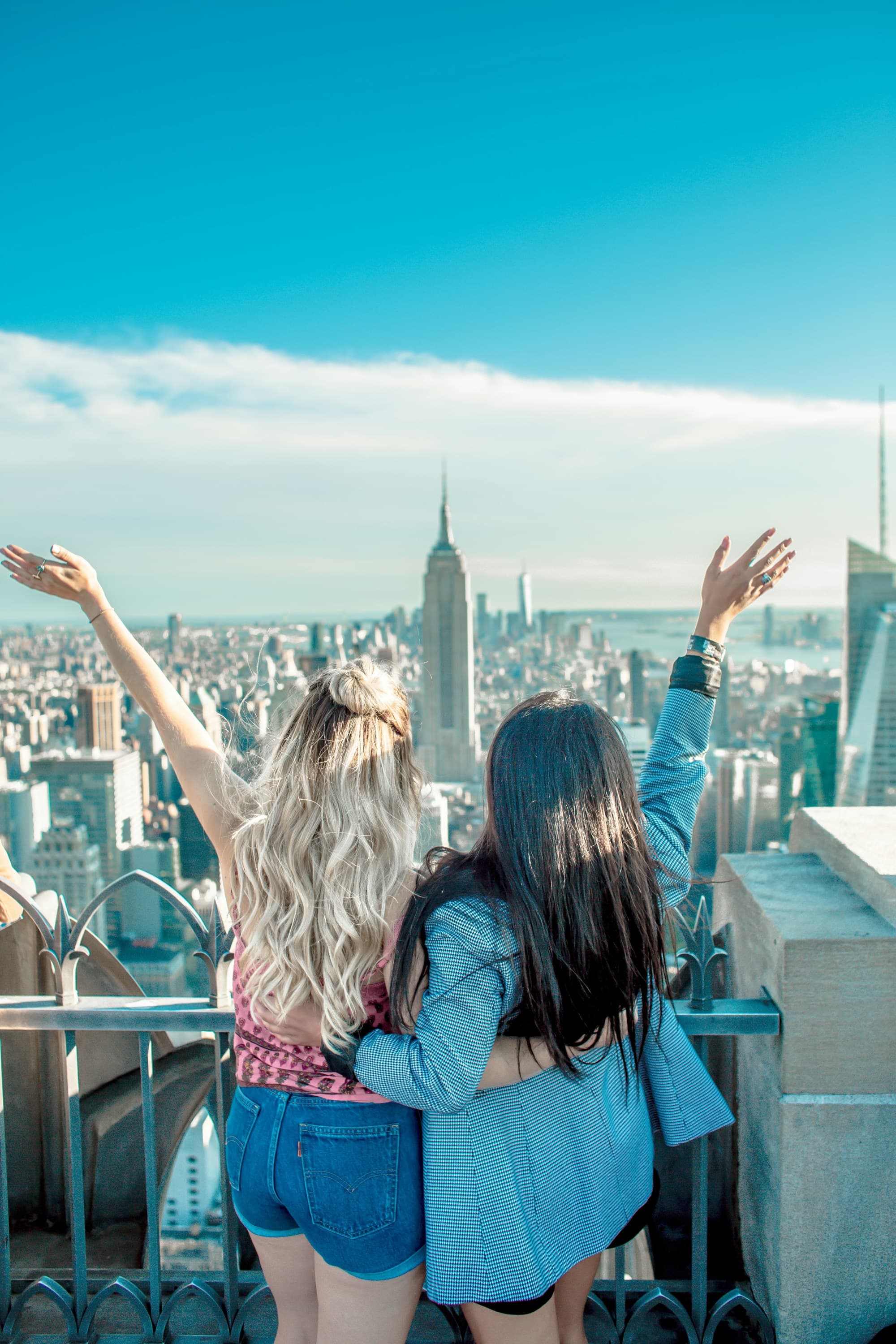 Two friends posing for a photo with their backs to the camera and a view of the Manhattan skyline in the background