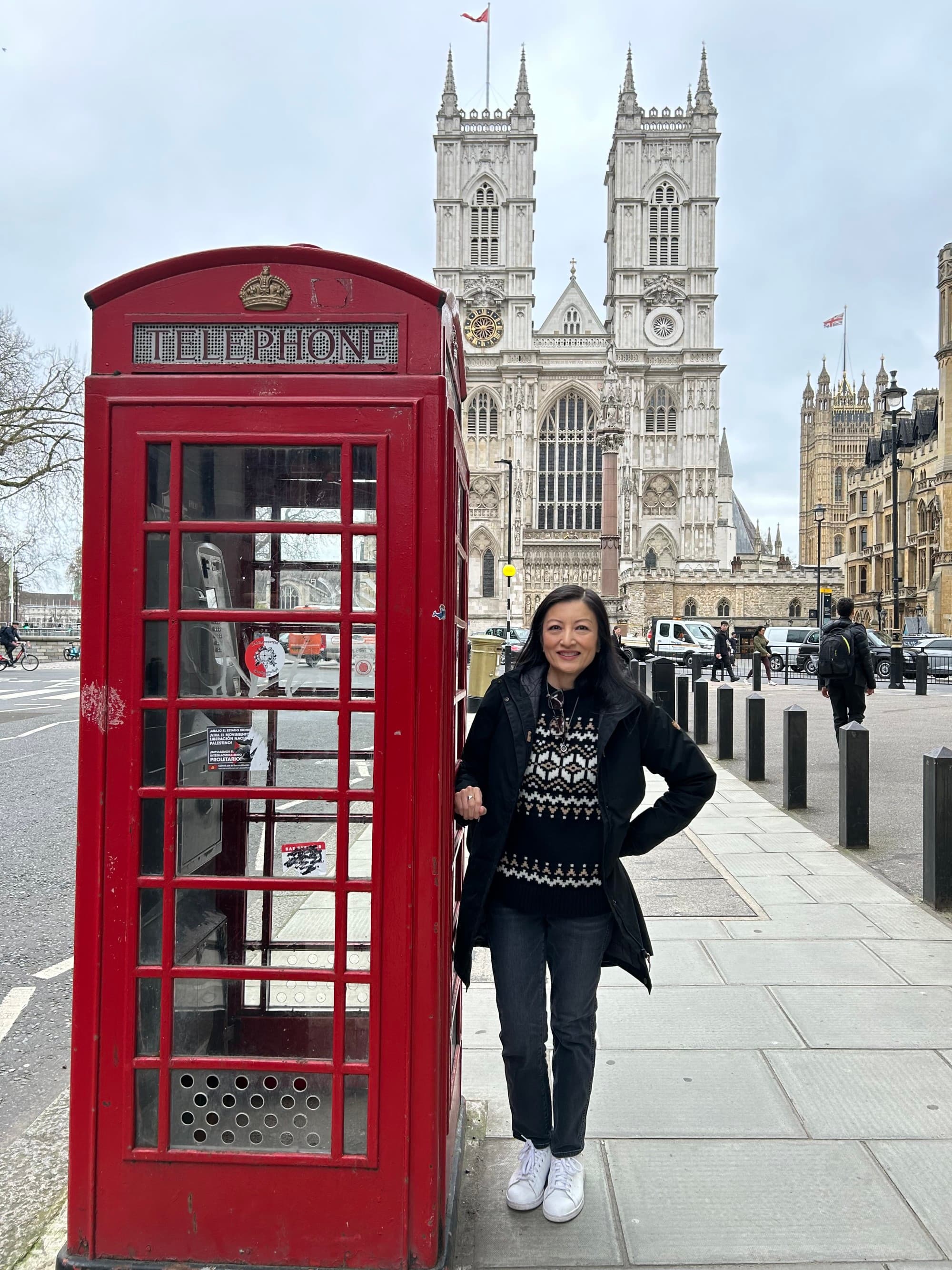 An image of a woman posing next to a red telephone booth with a large stone cathedral in the background, near some of the best places for shopping in London.