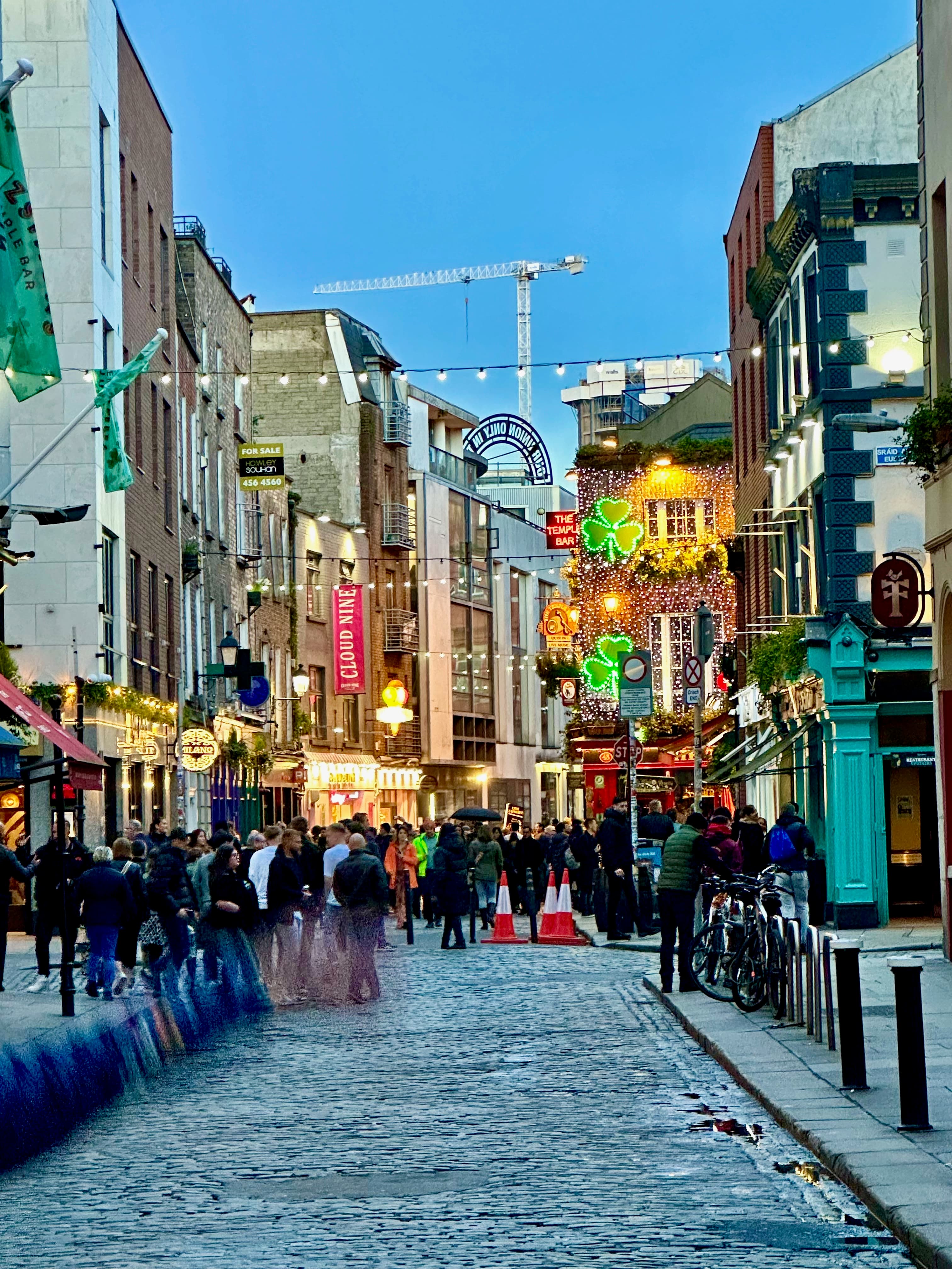 Cobblestone city streets in Dublin in the evening with neon shamrocks and people walking around.