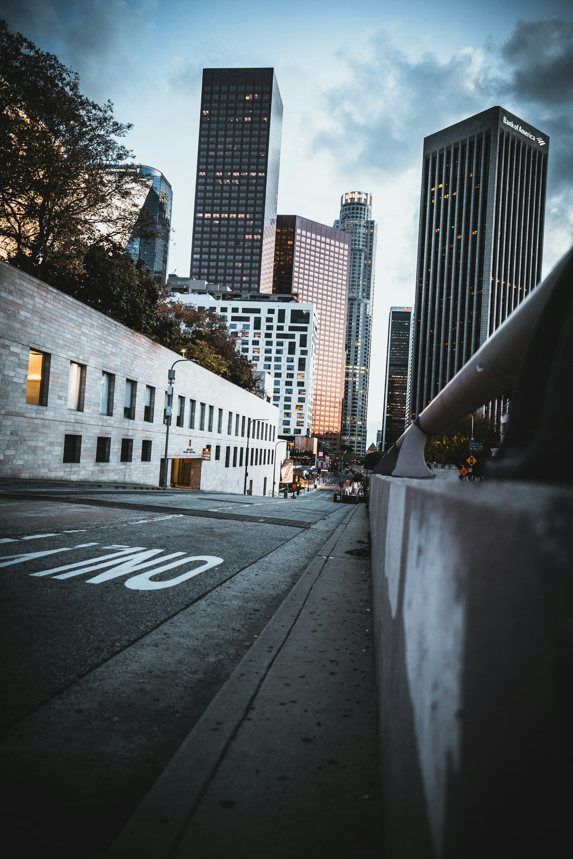 This image depicts a street view of downtown Los Angeles with skyscrapers, warehouse style buildings and trees in frame.