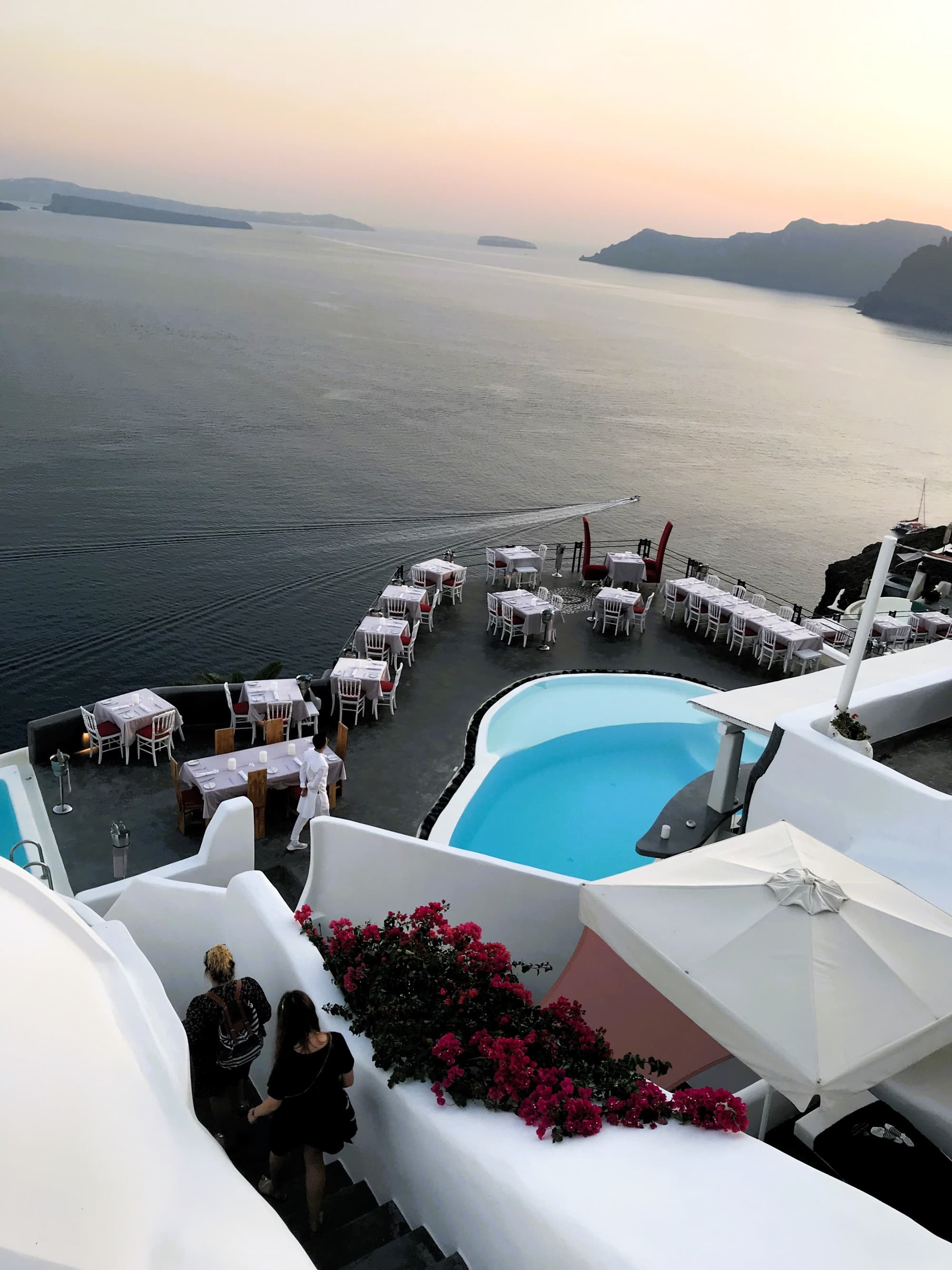 A restaurant patio directly overlooking the sea with white Greek-style stairs going down to it.