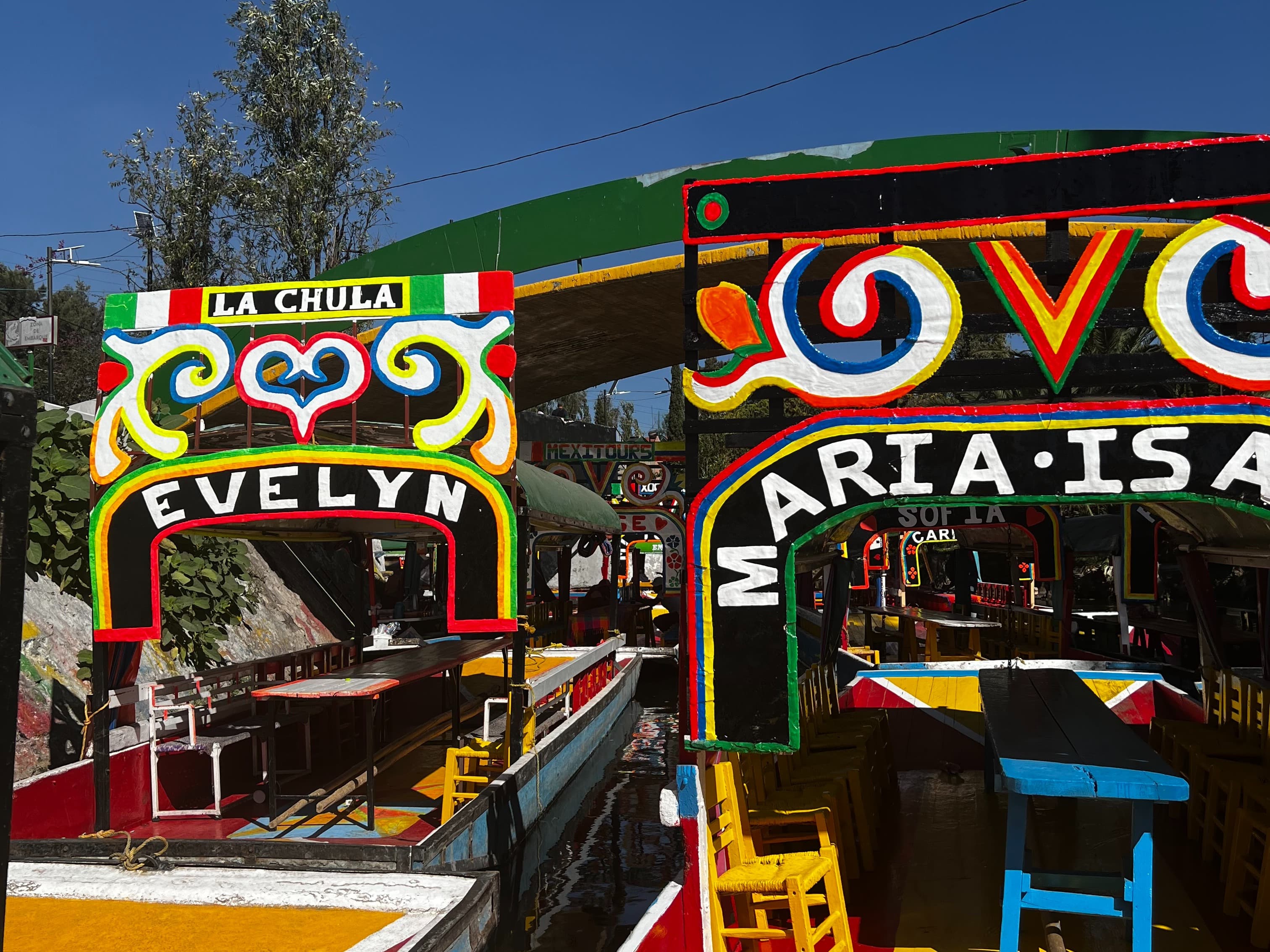 An image of two colorful archways and outdoor seating. There are trees and a blue sky in the background.