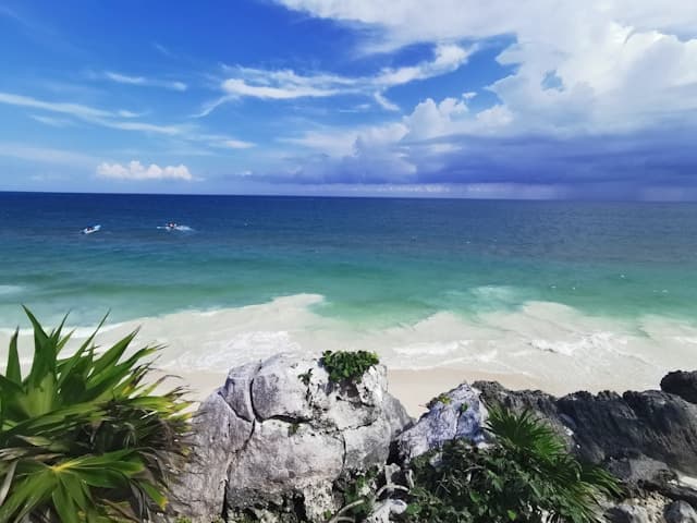 A view of one of Tulum's beaches from behind the rocky coastline, on a sunny day.