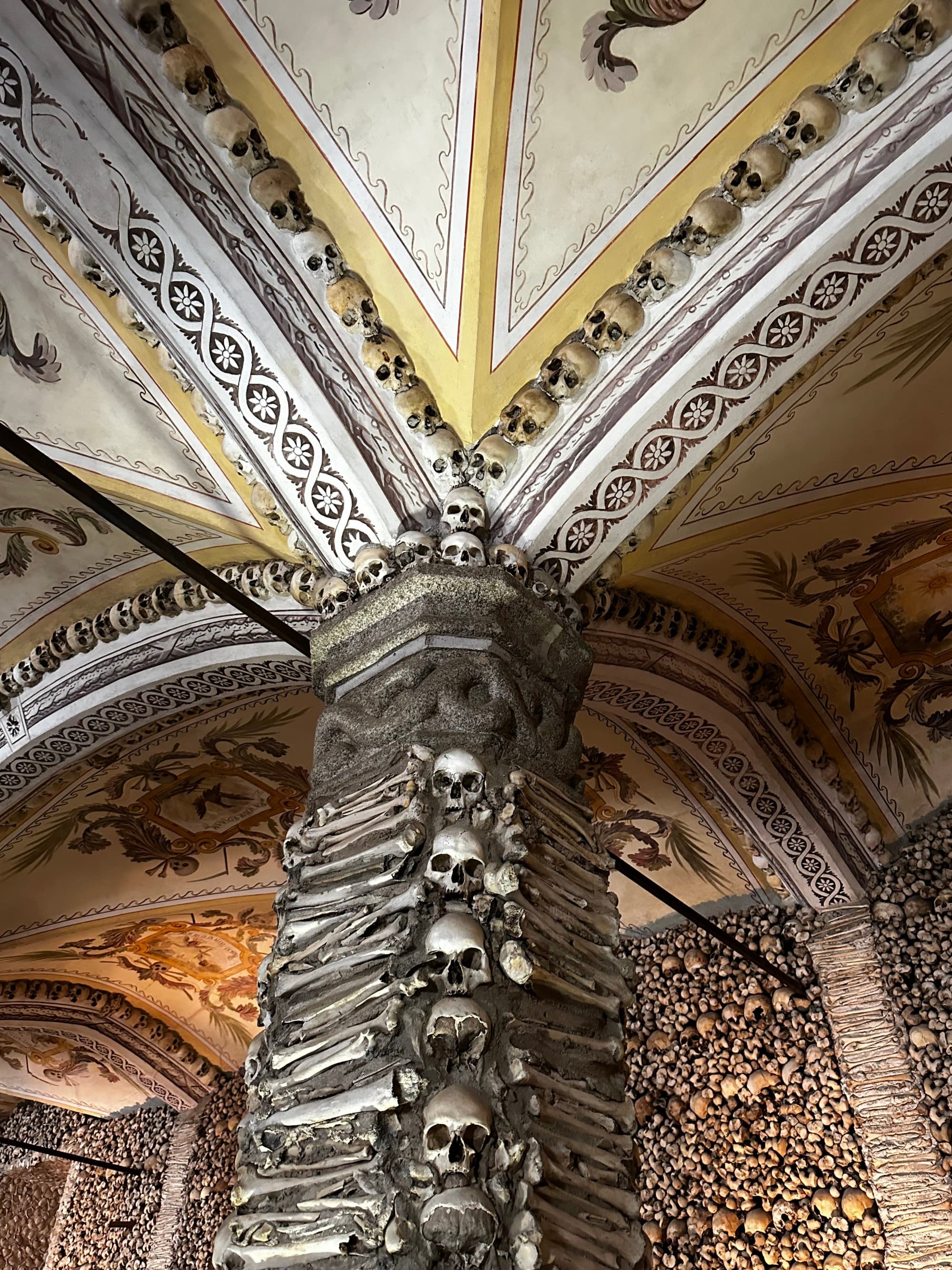 A pillar with skulls leading up to a beautifully painted ceiling with arches and patterns.