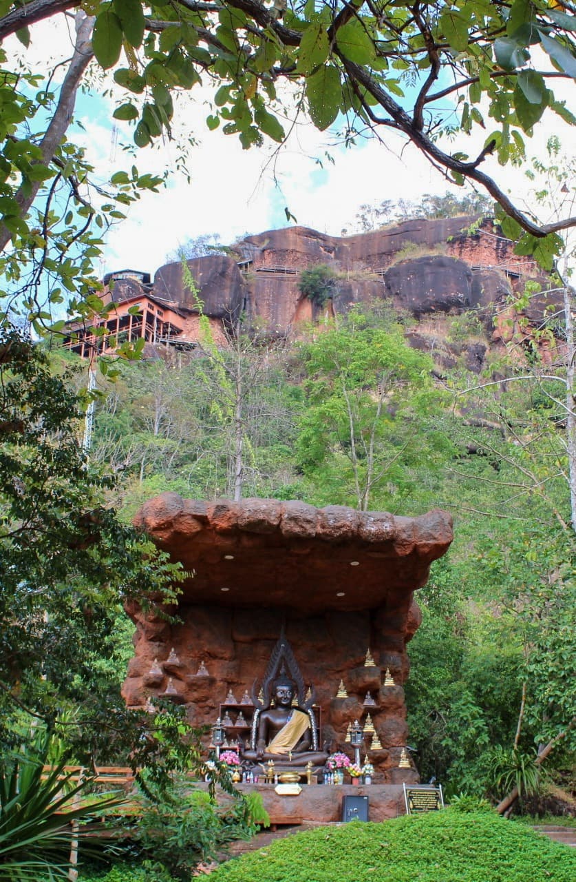 Outside of the temple of Wat Phu Tok, with green grass and trees on a sunny day.