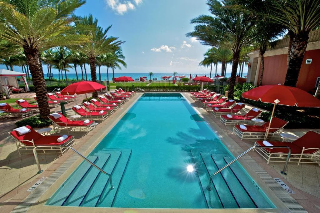 palm trees surrounding a pool and the beach in the distance