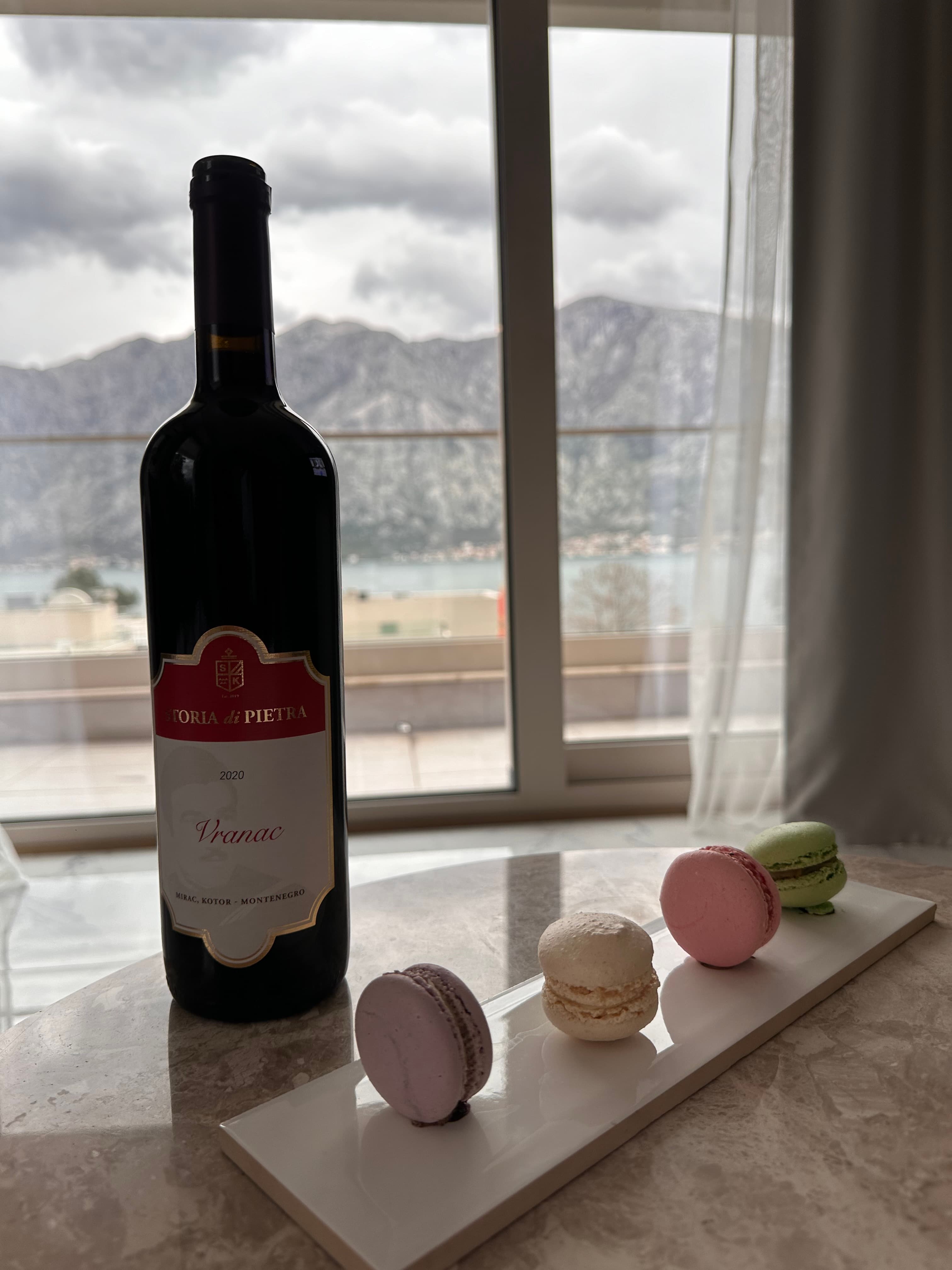 A picture of a bottle of wine and macarons on a white dish placed on top of a stone table.