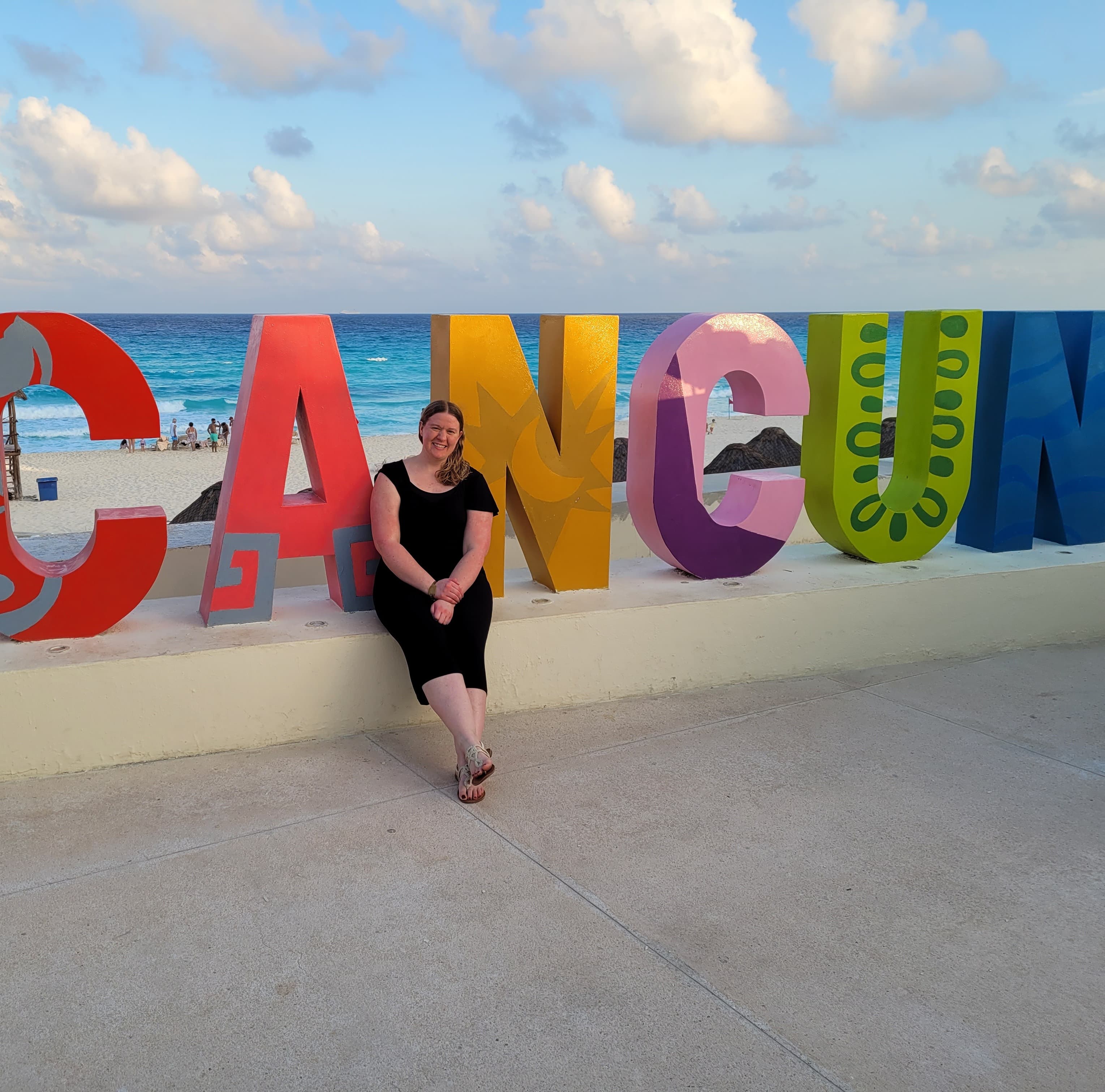 Advisor posing in front of a colorful sign reading "Cancun"
