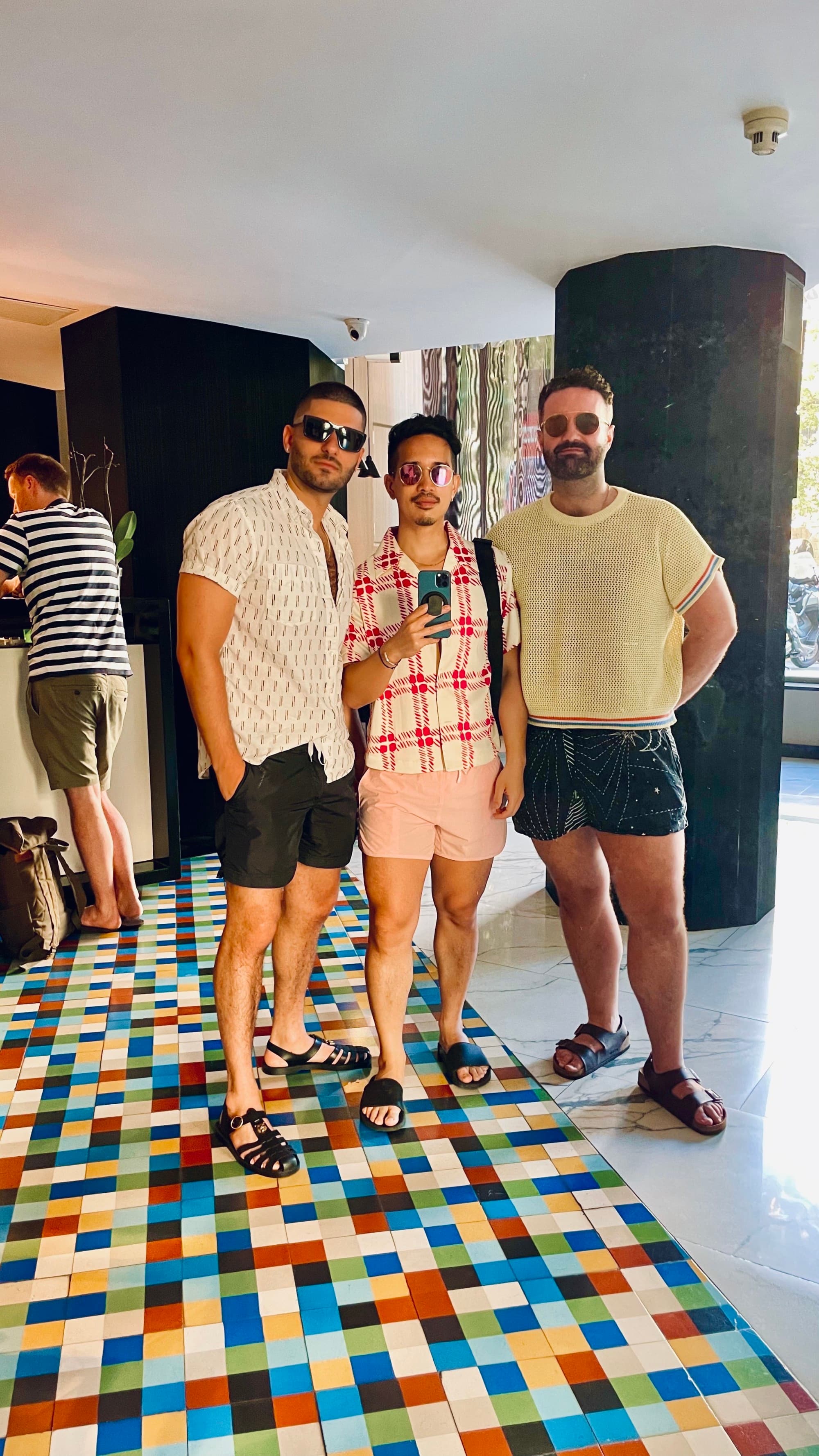 Three men dressed in tshirts and shorts, wearing sunglasses, standing on a colorful floor.