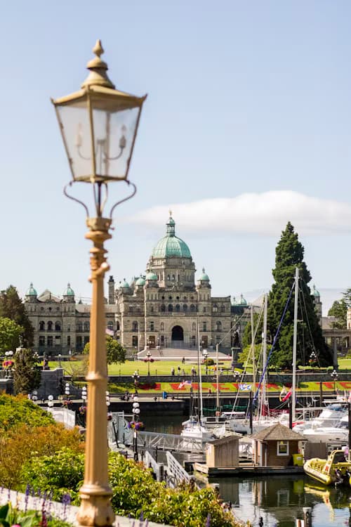 A light post in front of a harbor, trees, flowers and a large building in the background.