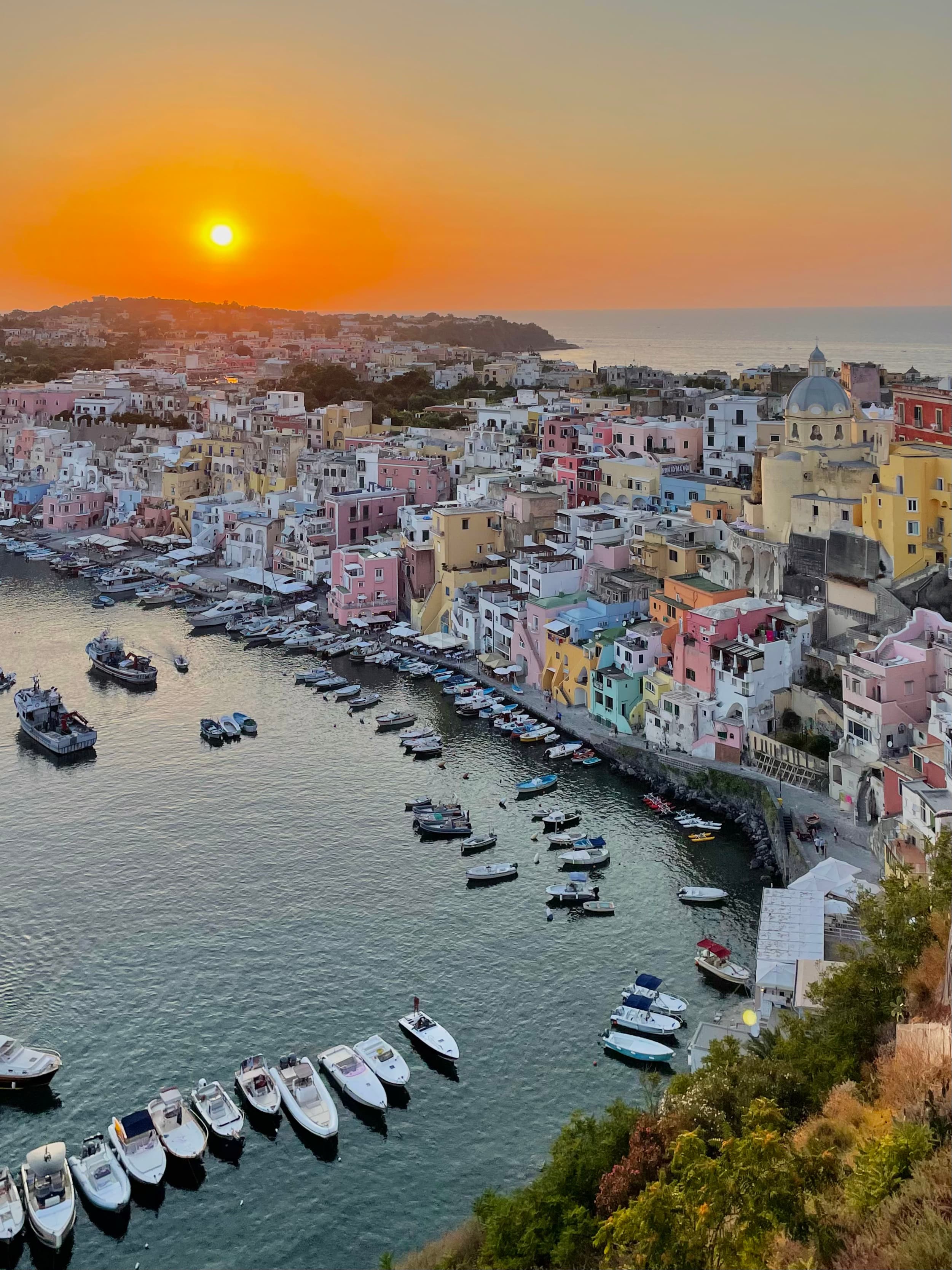 A picture of a beautiful coastline with colorful houses and boats in the water at sunset.