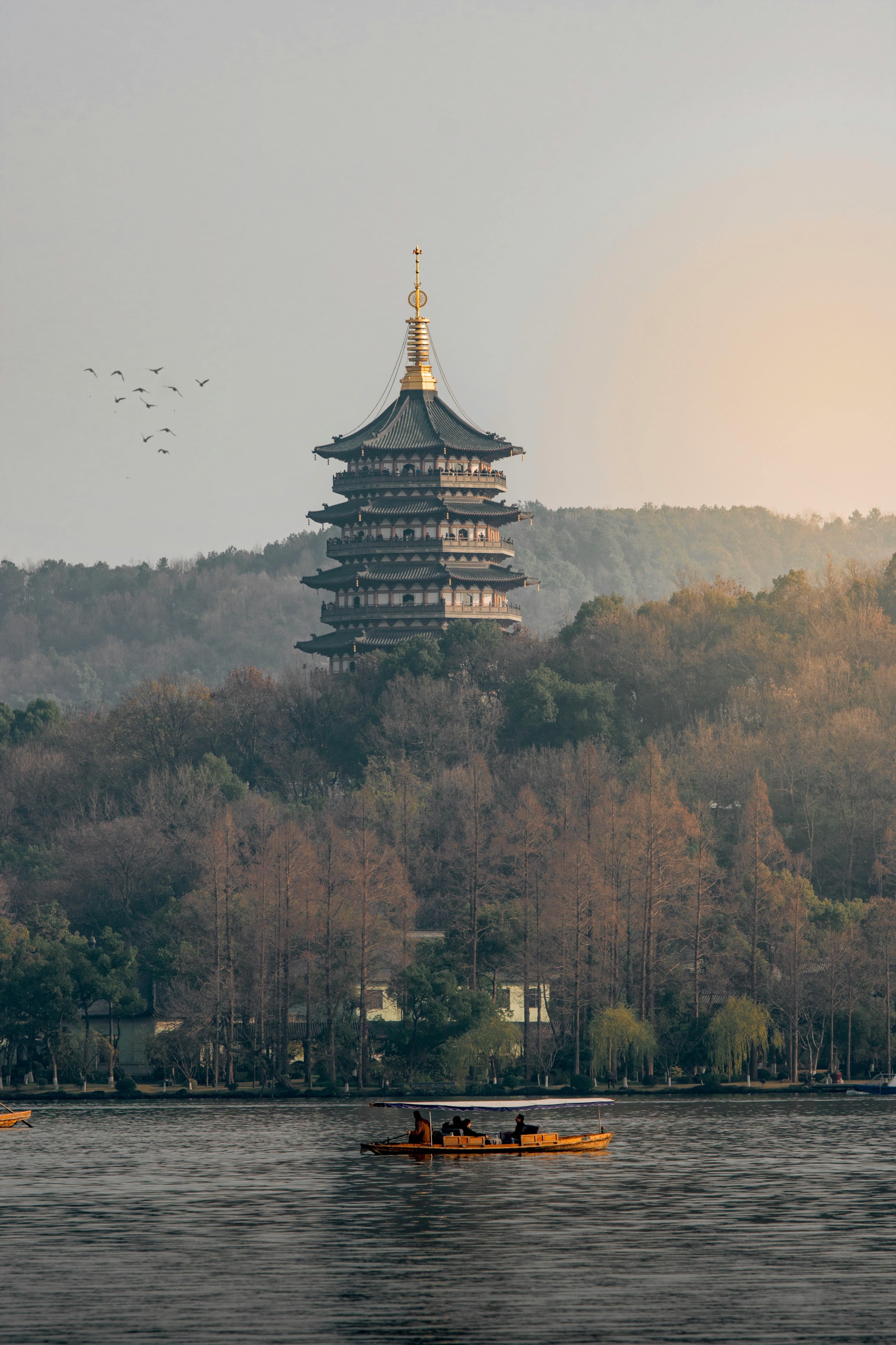 A calm river in China with a fishing boat sailing in the water. In the distance a multilevel temple with foliage surrounding.