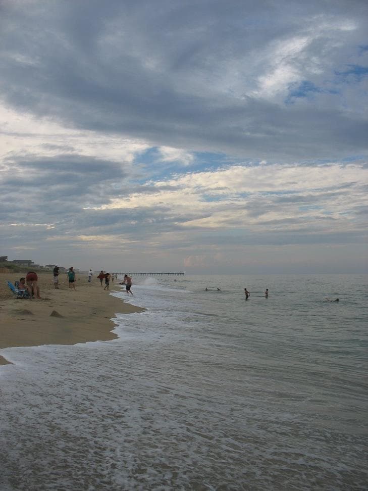 A long view of Outer Banks beach with people swimming and walking and clouds ahead