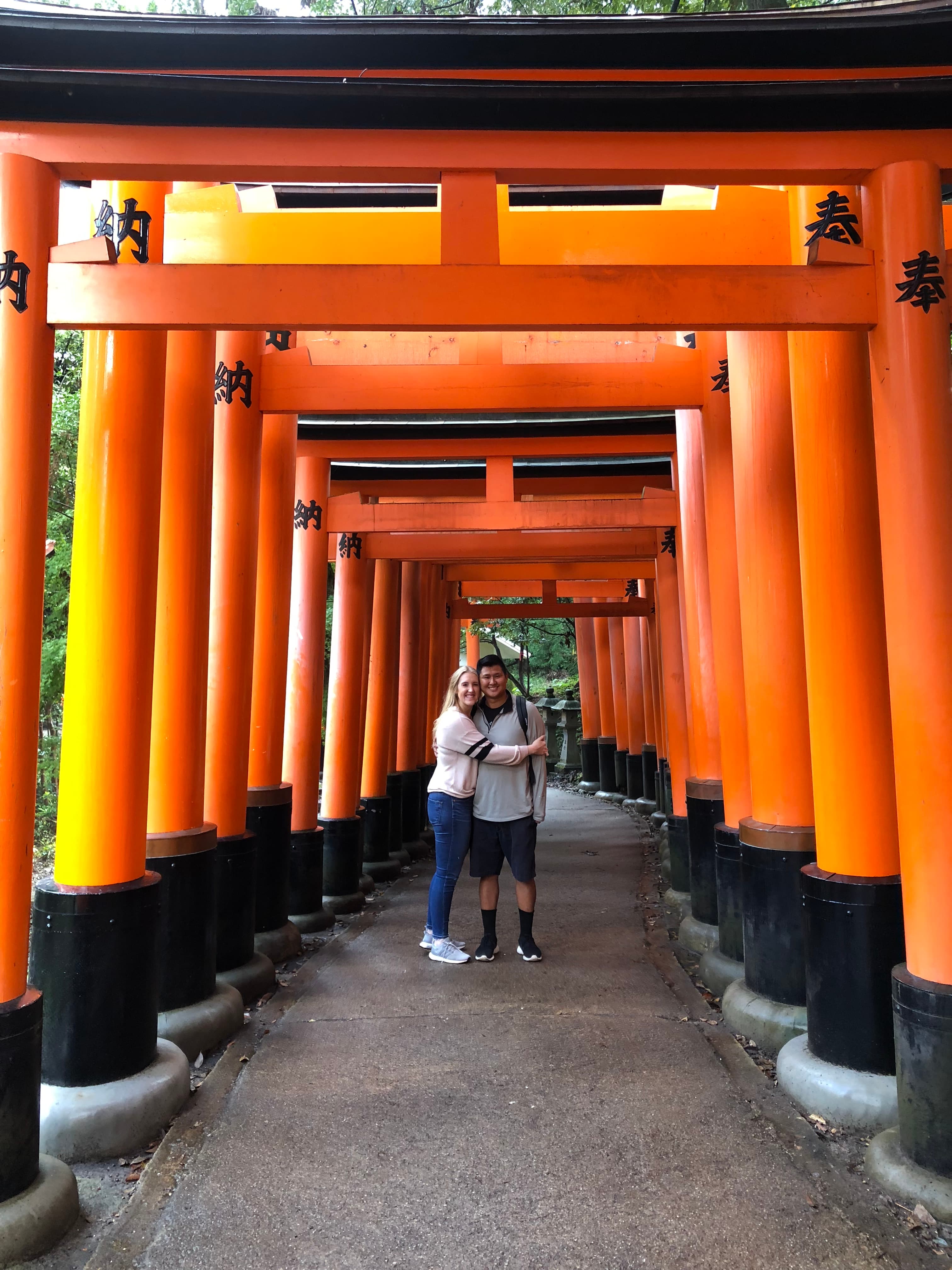 Two people posing beneath the red arches of the Fushimi Inari Shrine.