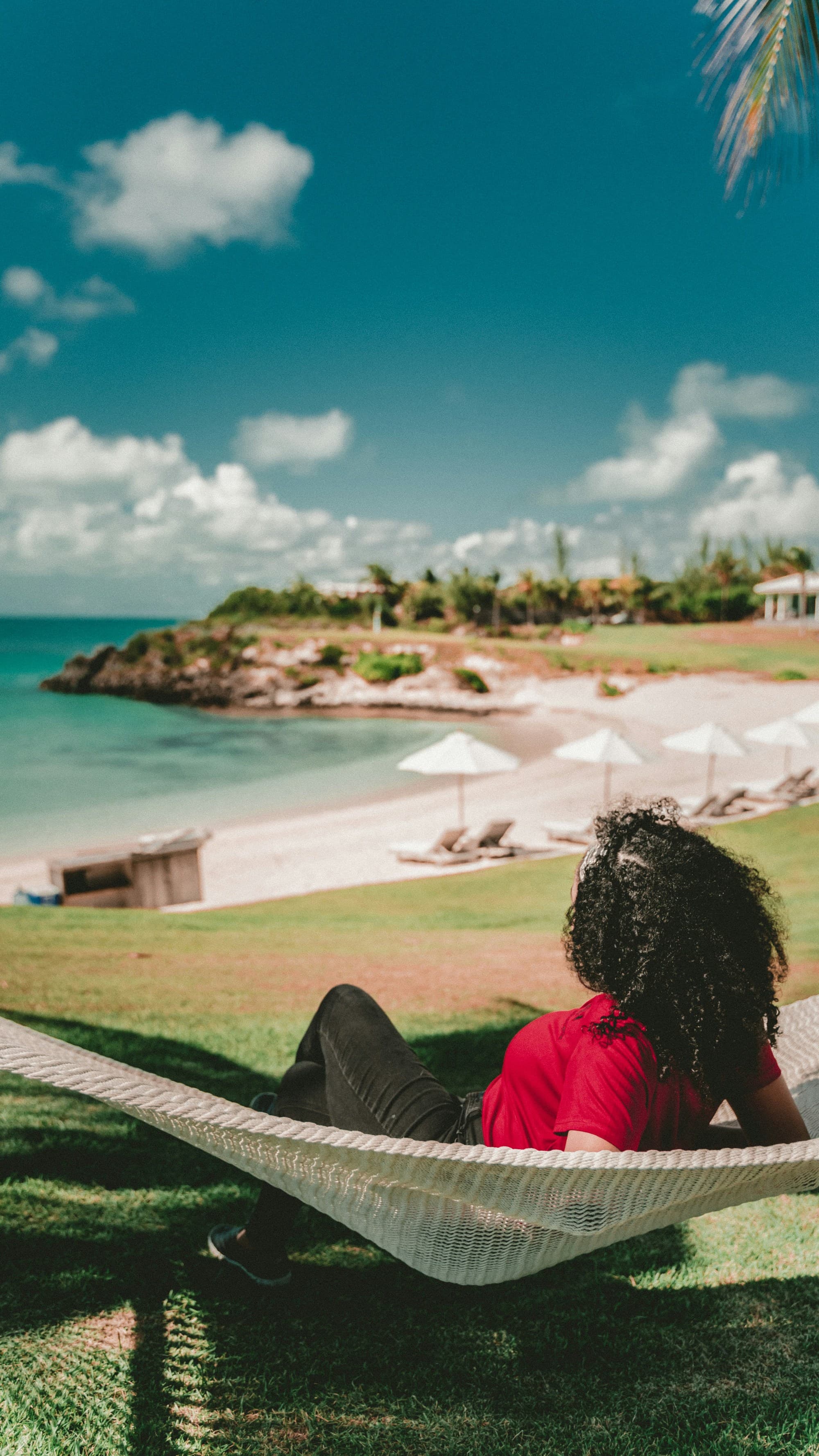 A picture of a woman lying on a hammock near the beach.