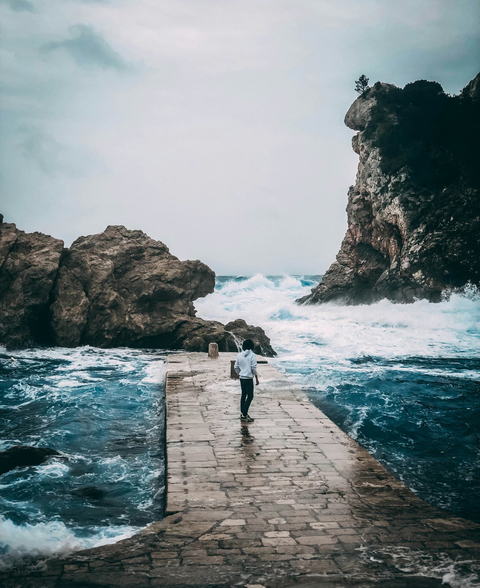 A picture of a woman in a white shirt and black pants on a concrete pathway near the sea during the daytime.
