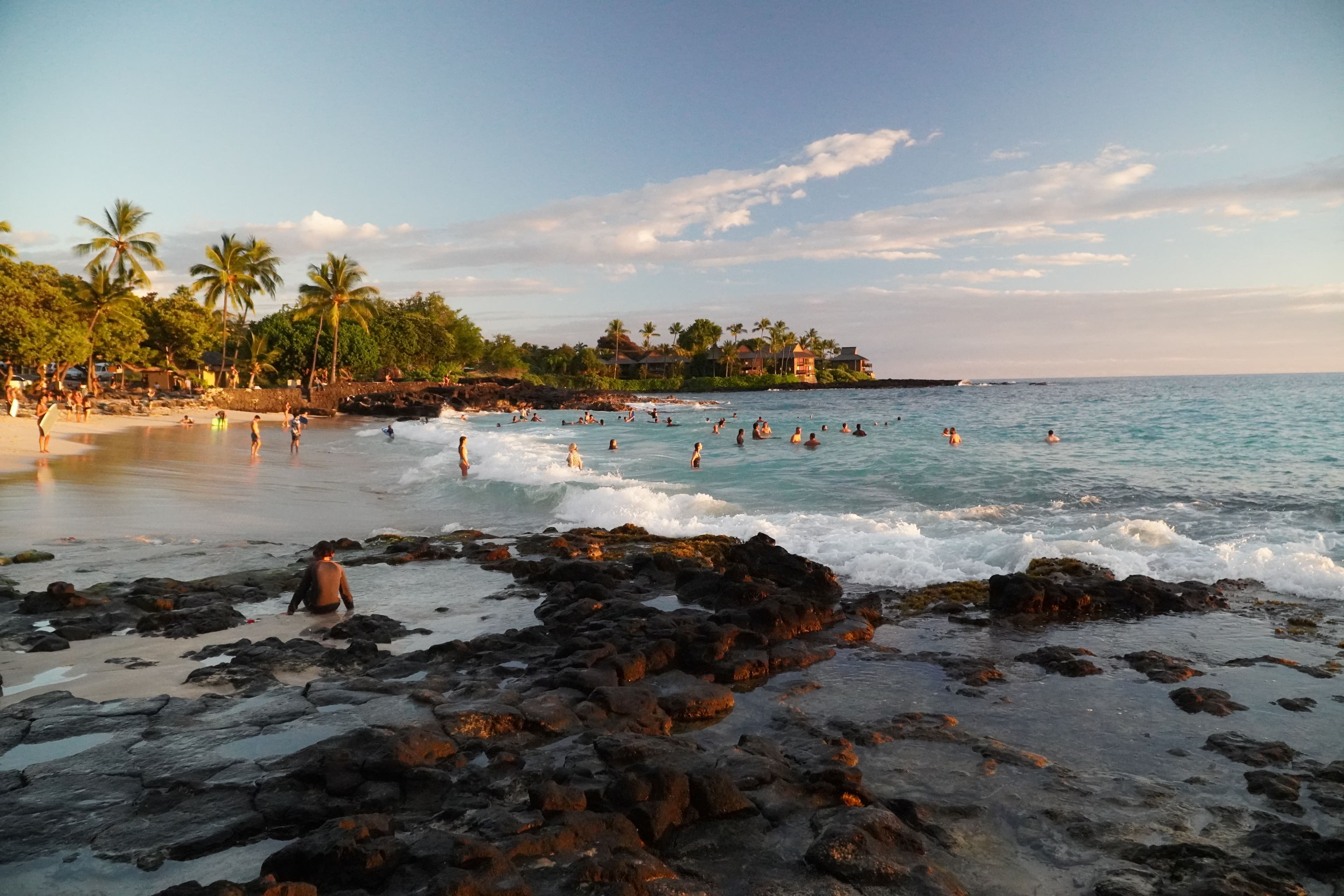 A beach in Hawaii with people standing in the surf and palm trees in the background.