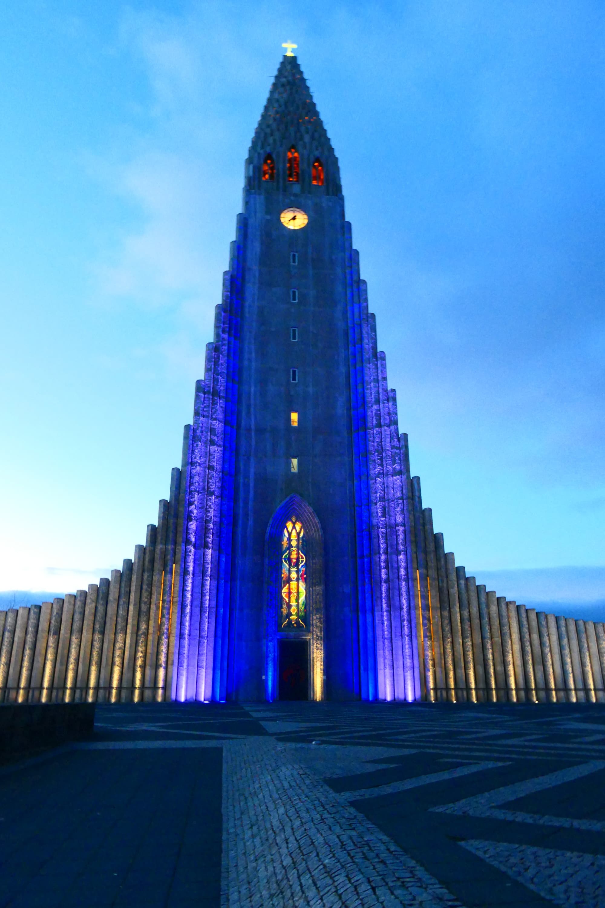 A picture of a tall building with purple-colored lights taken in the evening.