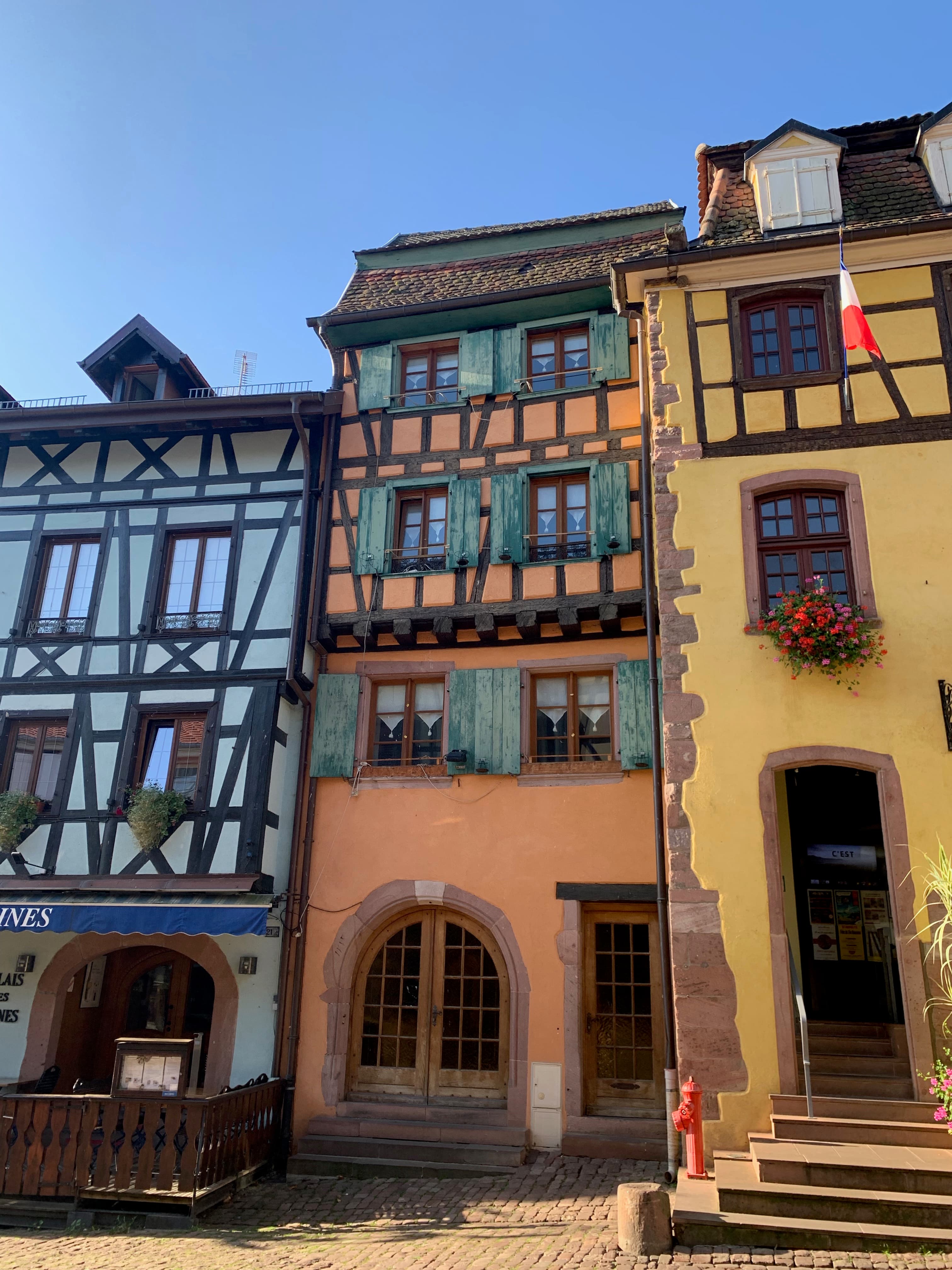 A white, orange and yellow colored set of three buildings with shutters and wood paneling.