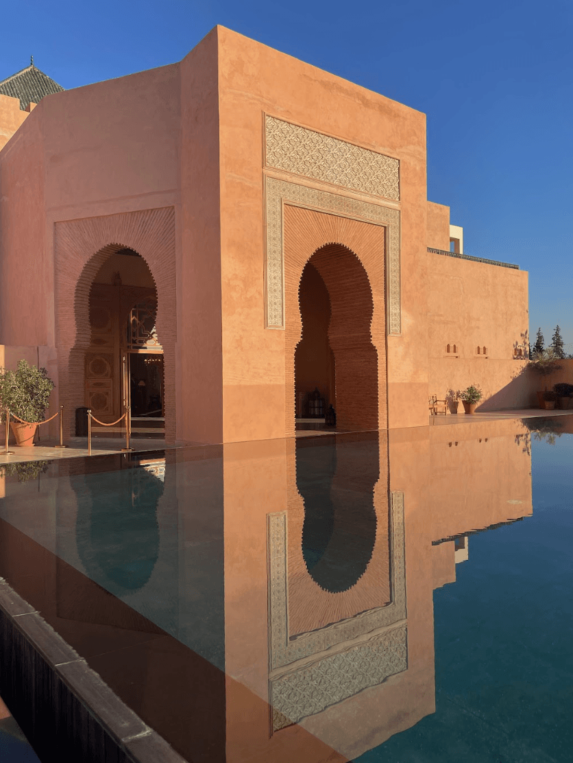 A stunning light pink building with arches near a reflective pool beneath the clear blue sky.