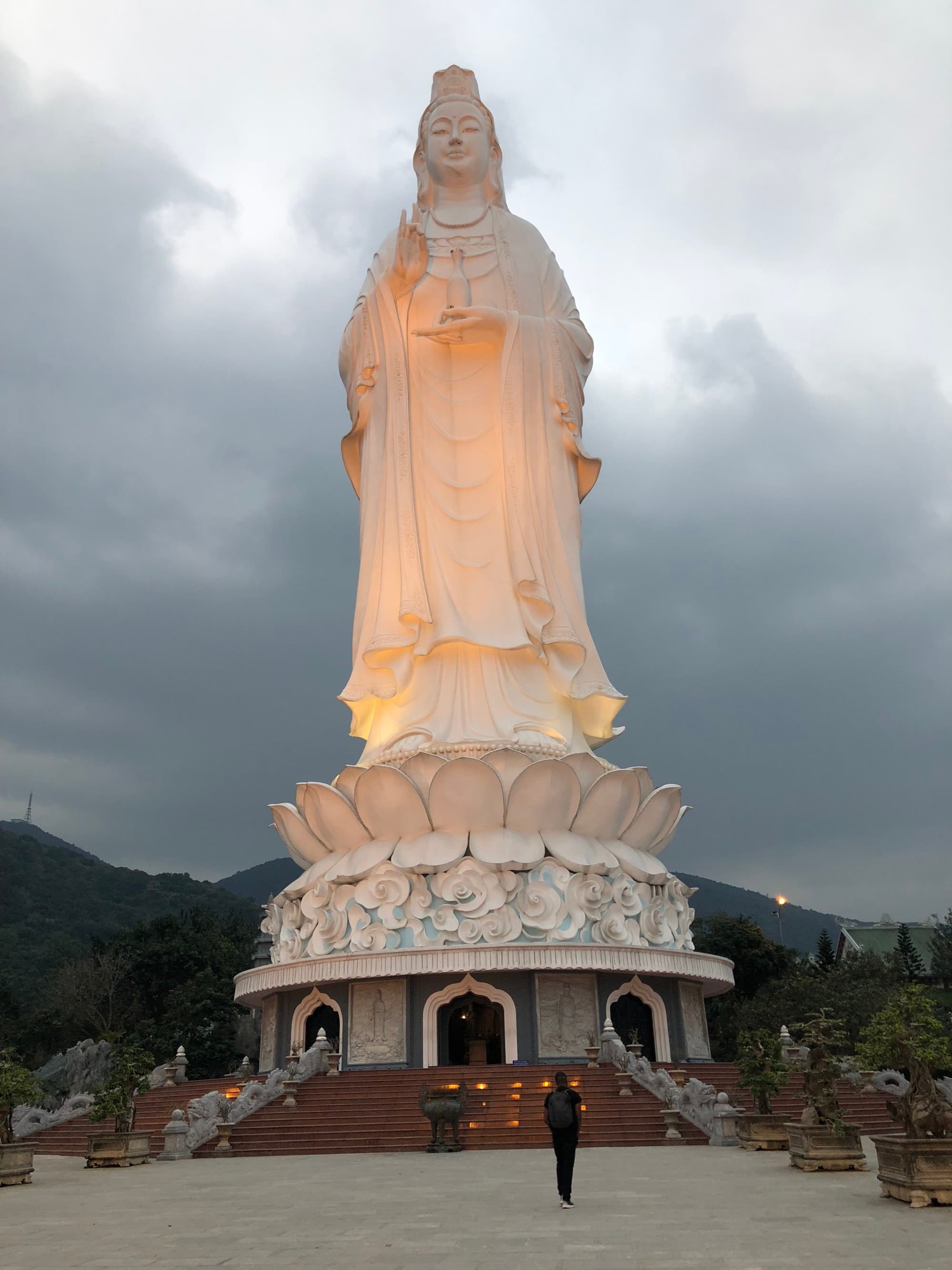 A low-angled shot of a Lady Buddha statue made out of a white stone and lit up at daytime.