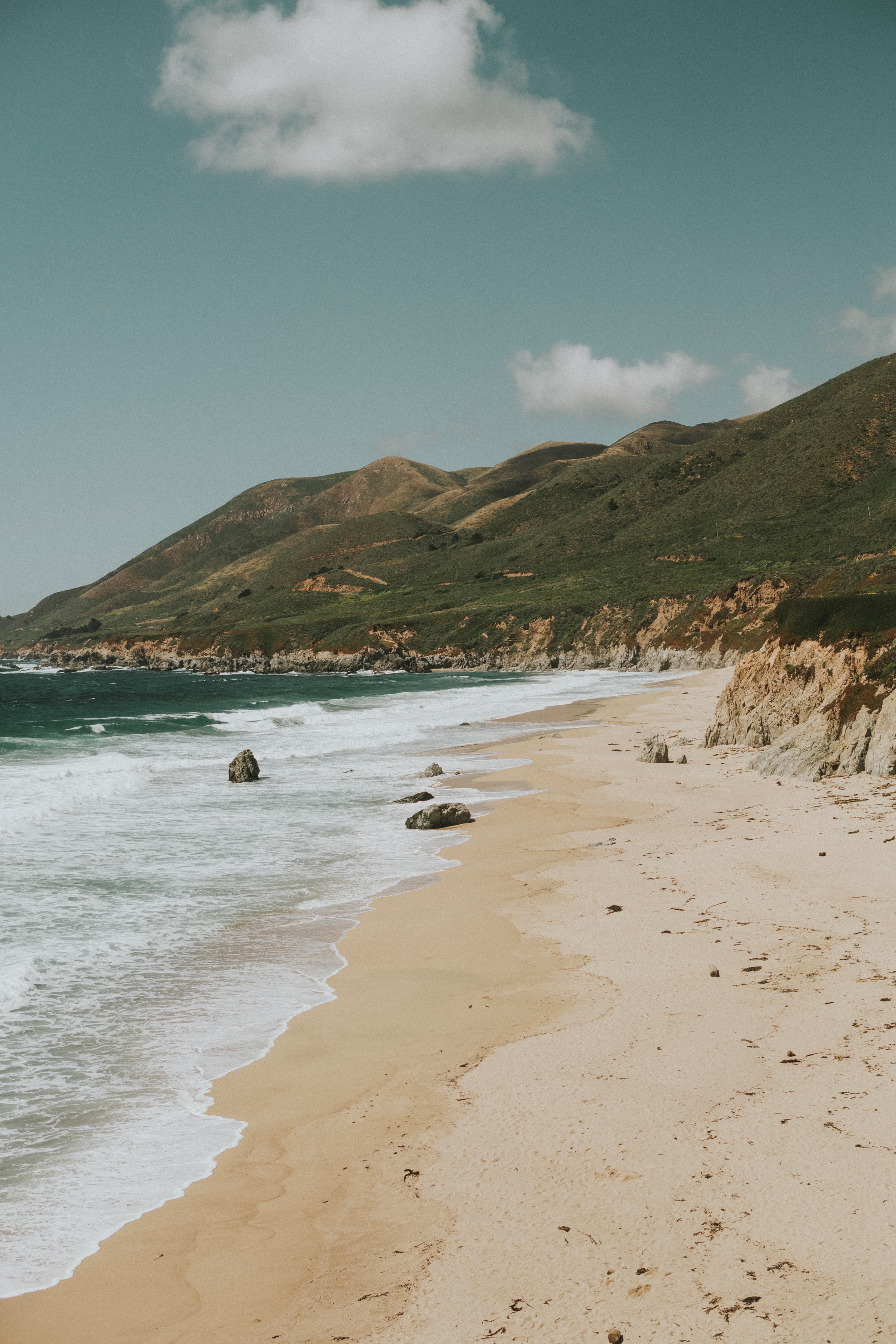 green hill next to sandy beach and ocean during daytime
